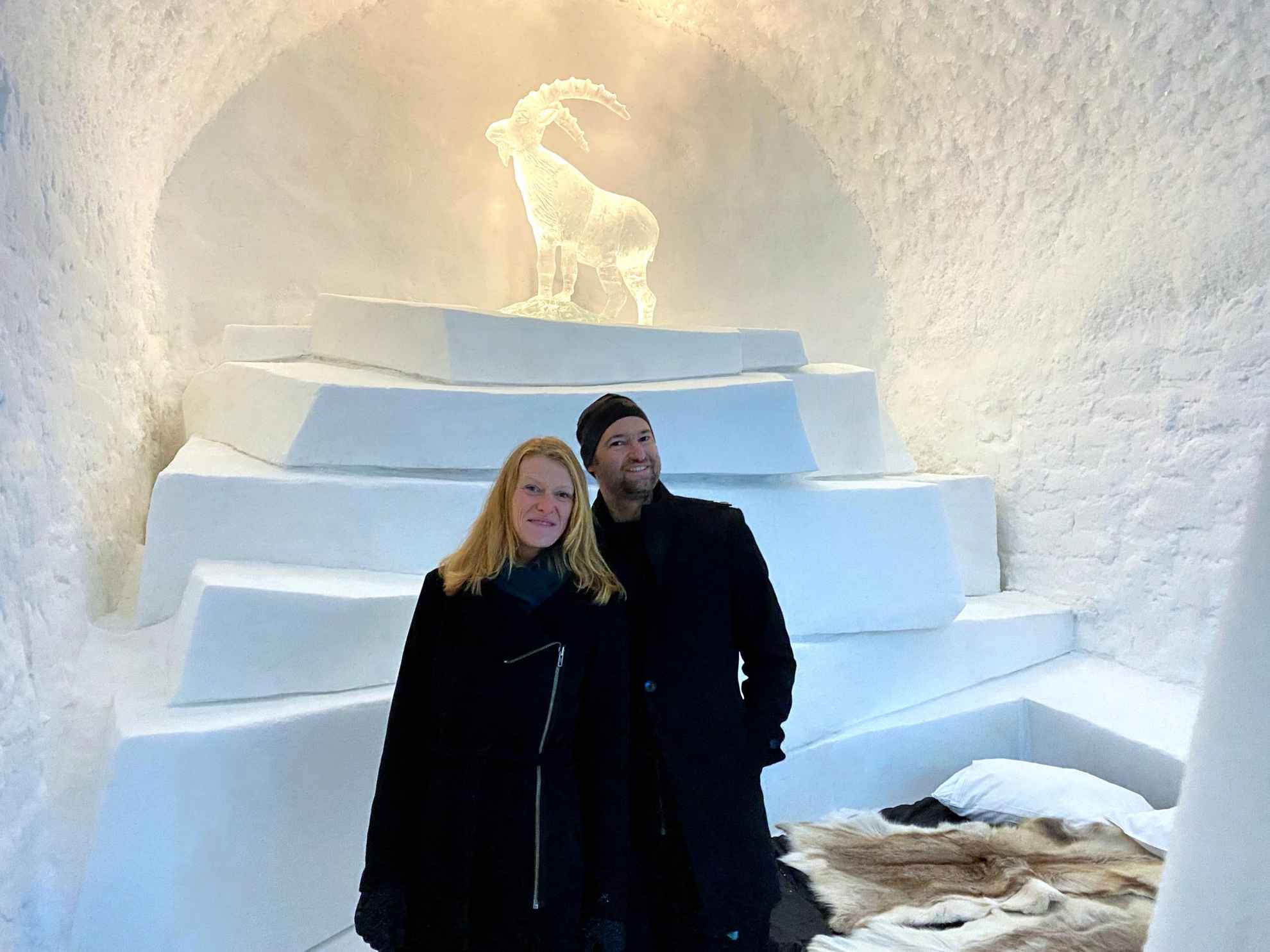 Eine Frau und ein Mann stehen vor einer Eisskulptur eines Steinbocks, in einem Raum aus Eis und Schnee.