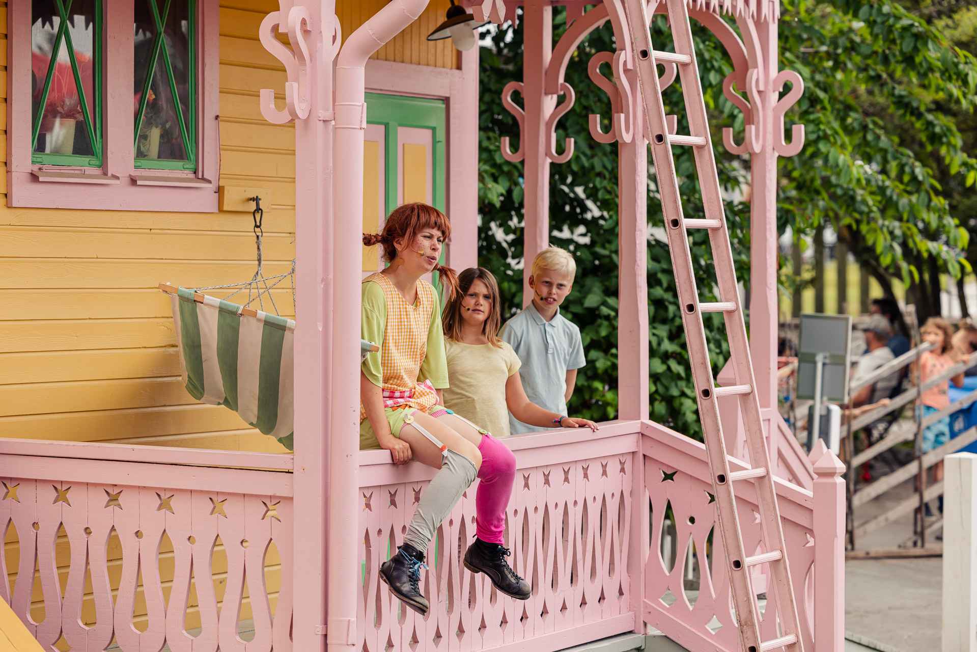 Eine Theateraufführung mit Pippi Langstrumpf, die auf der Veranda ihres gelben Hauses sitzt, Tommy und Annika stehen an ihrer Seite.