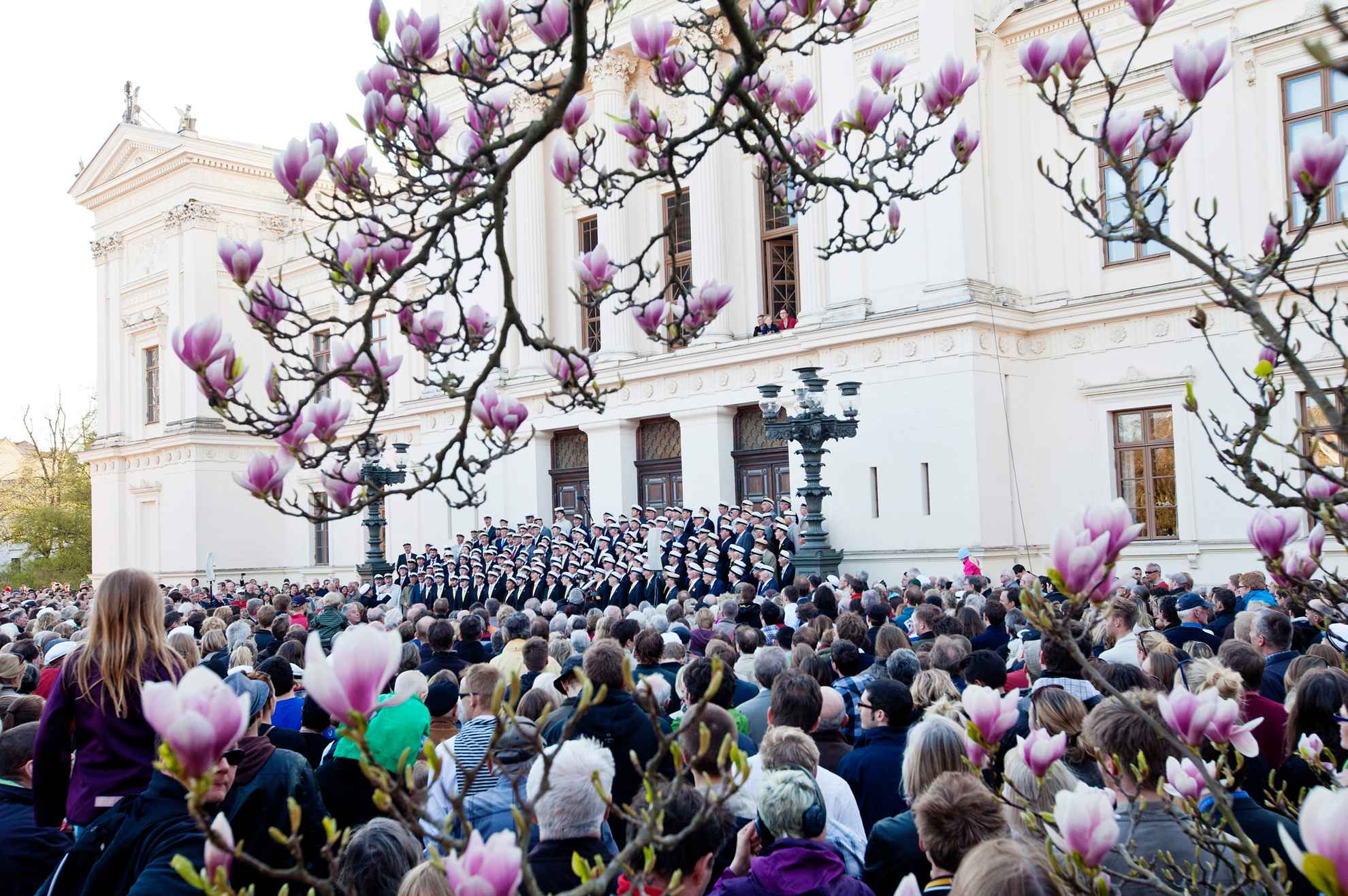 Studenten stehen vor dem Eingang eines Gebäutes der Lund Universität und singen. Viele Zuschauer stehen daneben.