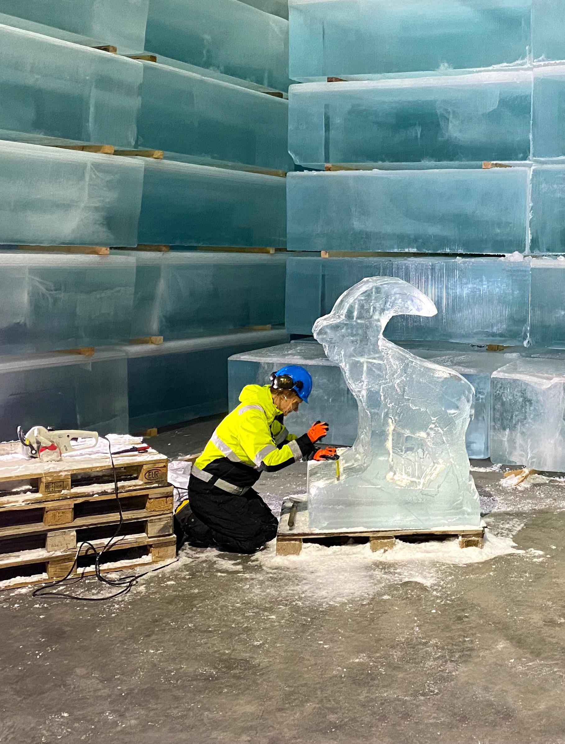 Eine Frau in Arbeitskleidung und mit Helm formt einen Steinbock aus Eis.