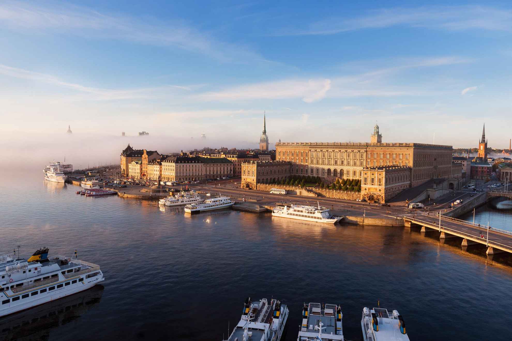 Luftaufnahme des königlichen Palastes und anderer Gebäude in der Stadt Stockholm. Am Hafen liegen Boote an.