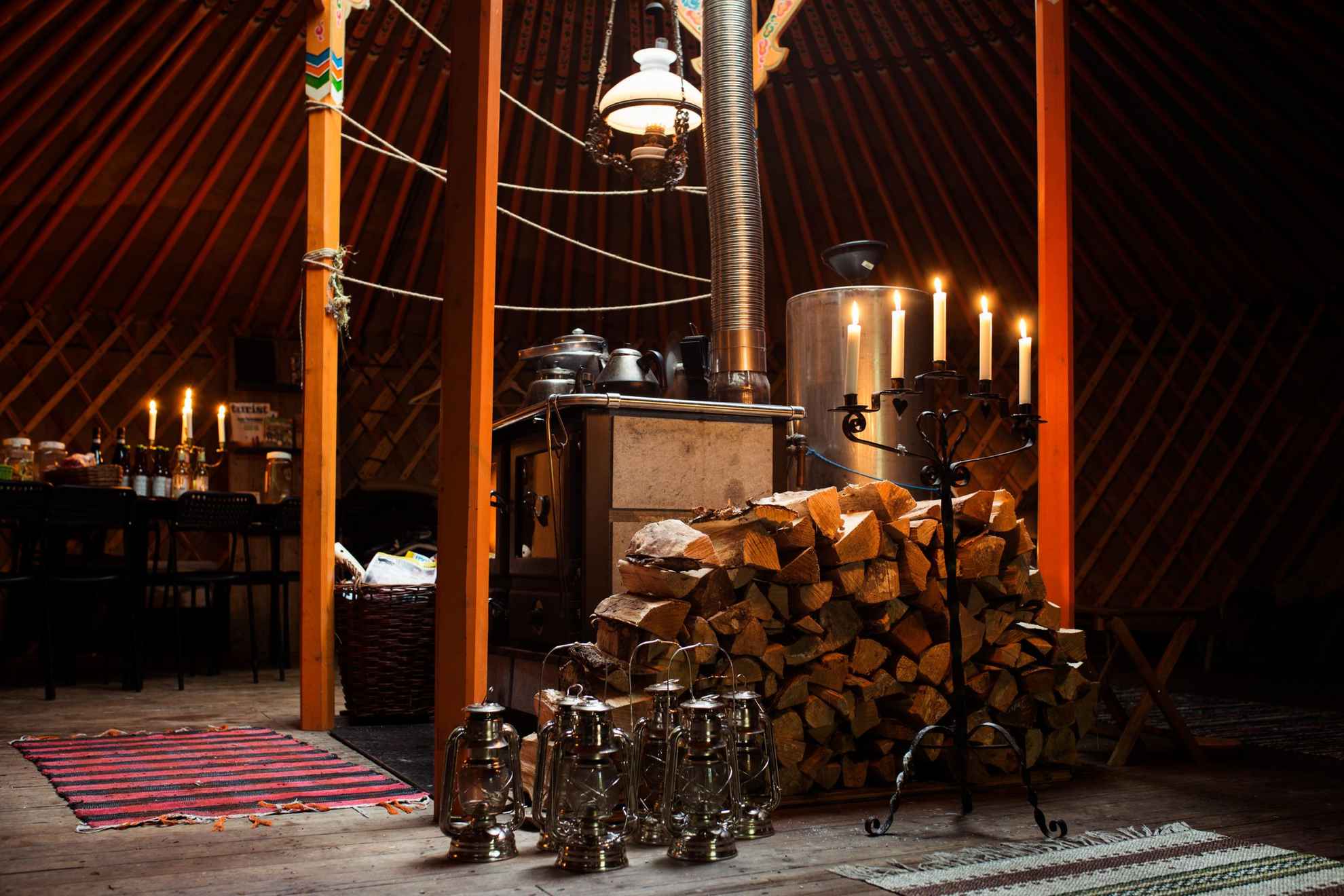 In einem großen Zelt steht ein Holzofen in dem Feuer gezündet ist. Kerzenschein sorgt zudem für eine gemütliche Atmosphäre.