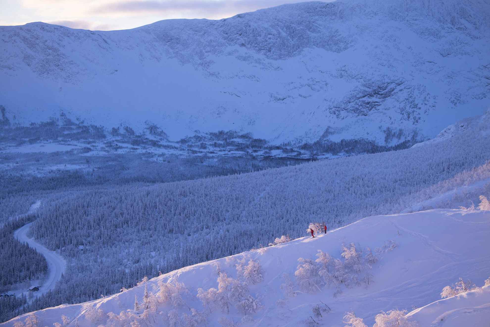 Eine malerischer Winterlandschaft. Zwei Personen fahren Ski und im Hintergrund ist ein Berg zu sehen.