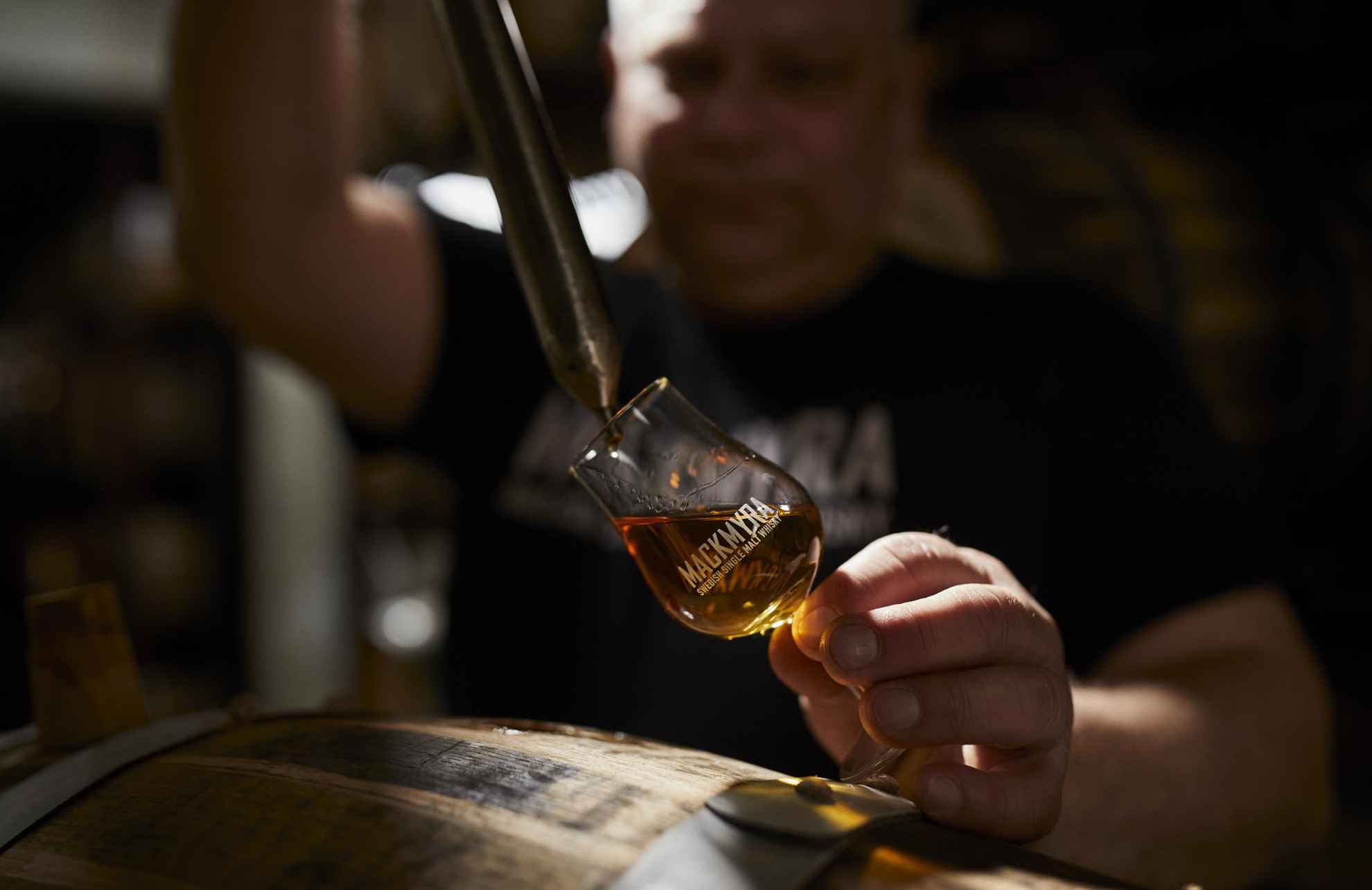 Whisky wird aus einer Pipette in ein Whiskyglas mit dem Text Mackmyra gegossen. Im Vordergrund steht ein Eichenfass.