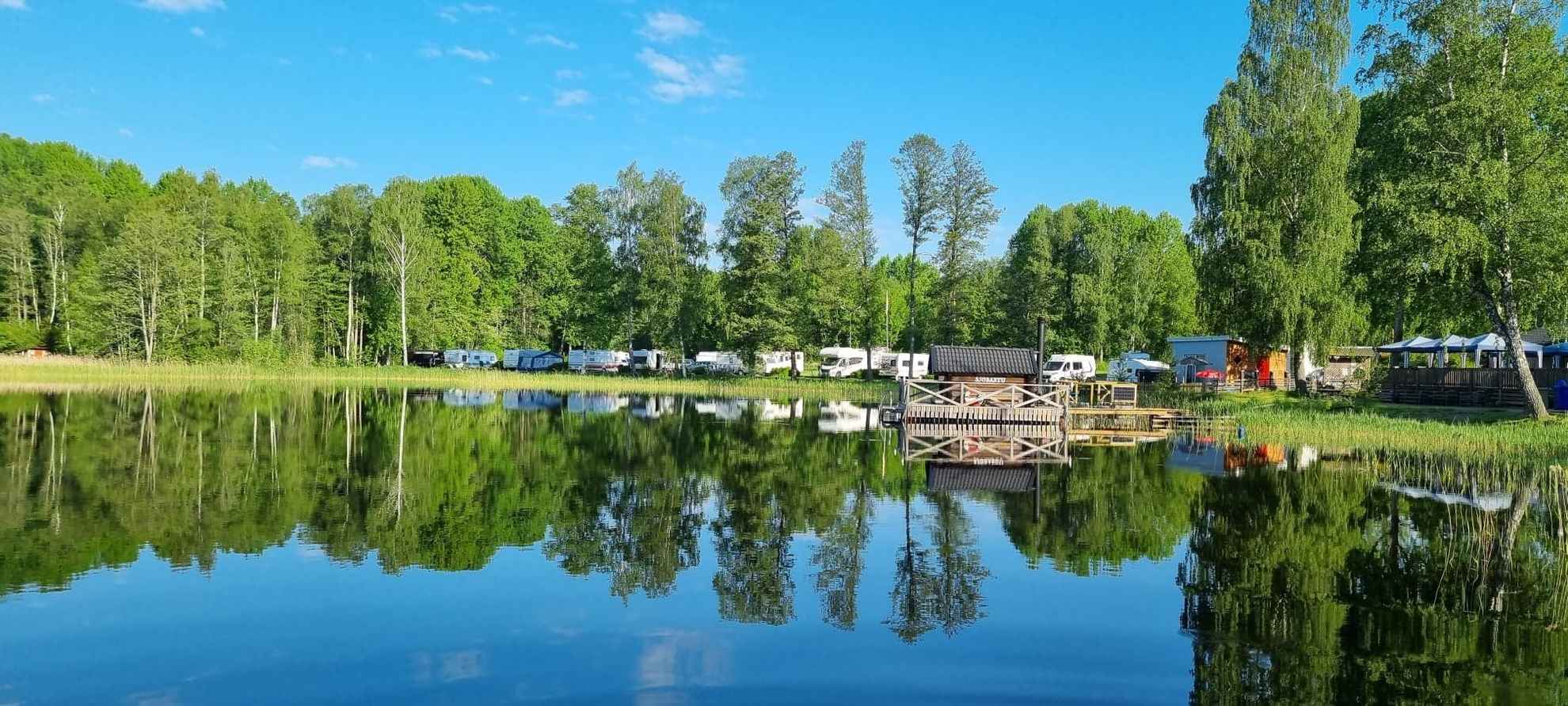 Im Wasser des Nossener Sees spiegeln sich die umliegenden Grünanlagen und die am Wasser geparkten Wohnmobile.