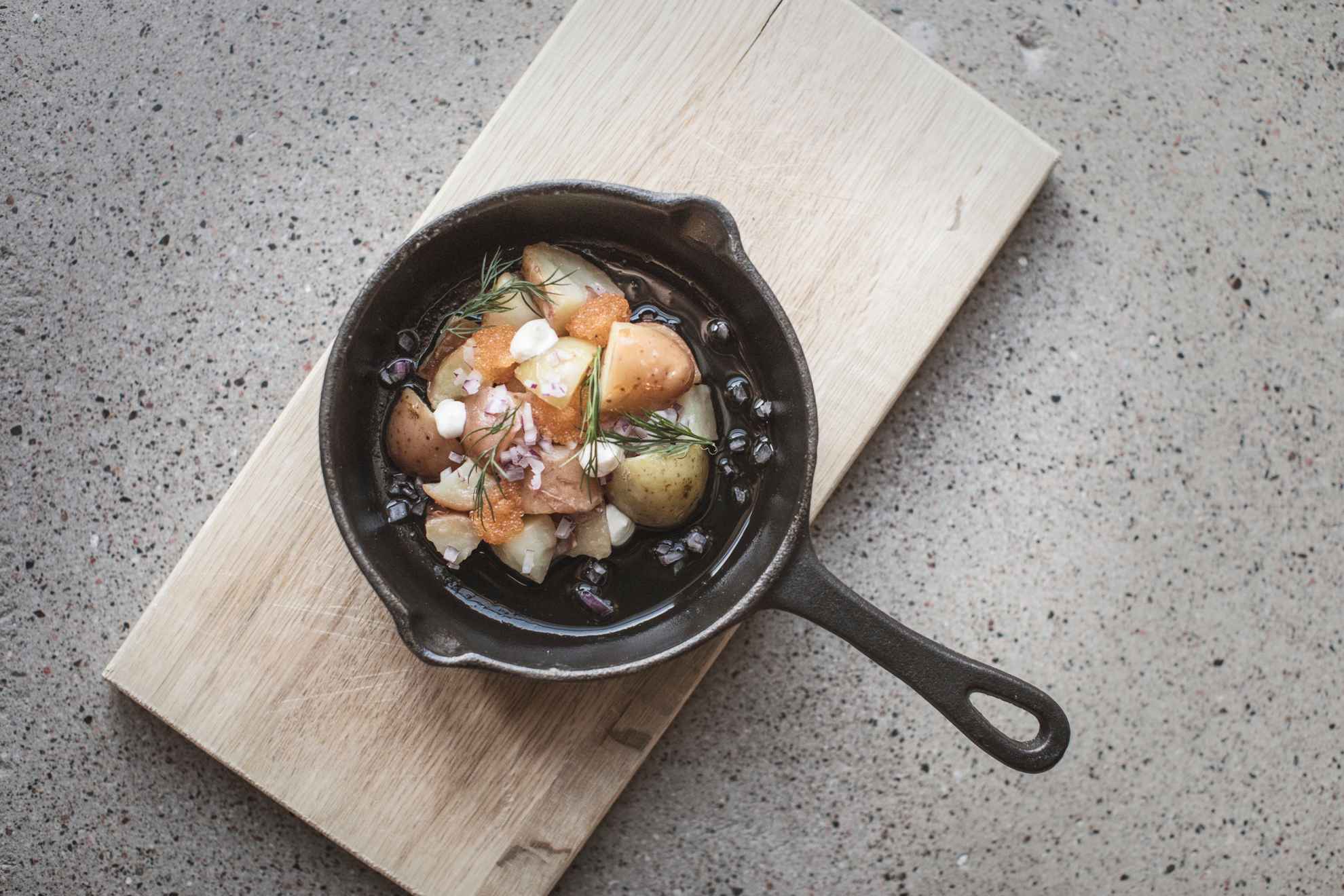 Nahaufnahme eines Gerichts mit Kaviar, der mit Kartoffeln und roten Zwiebeln in einer Eisenpfanne serviert wird.