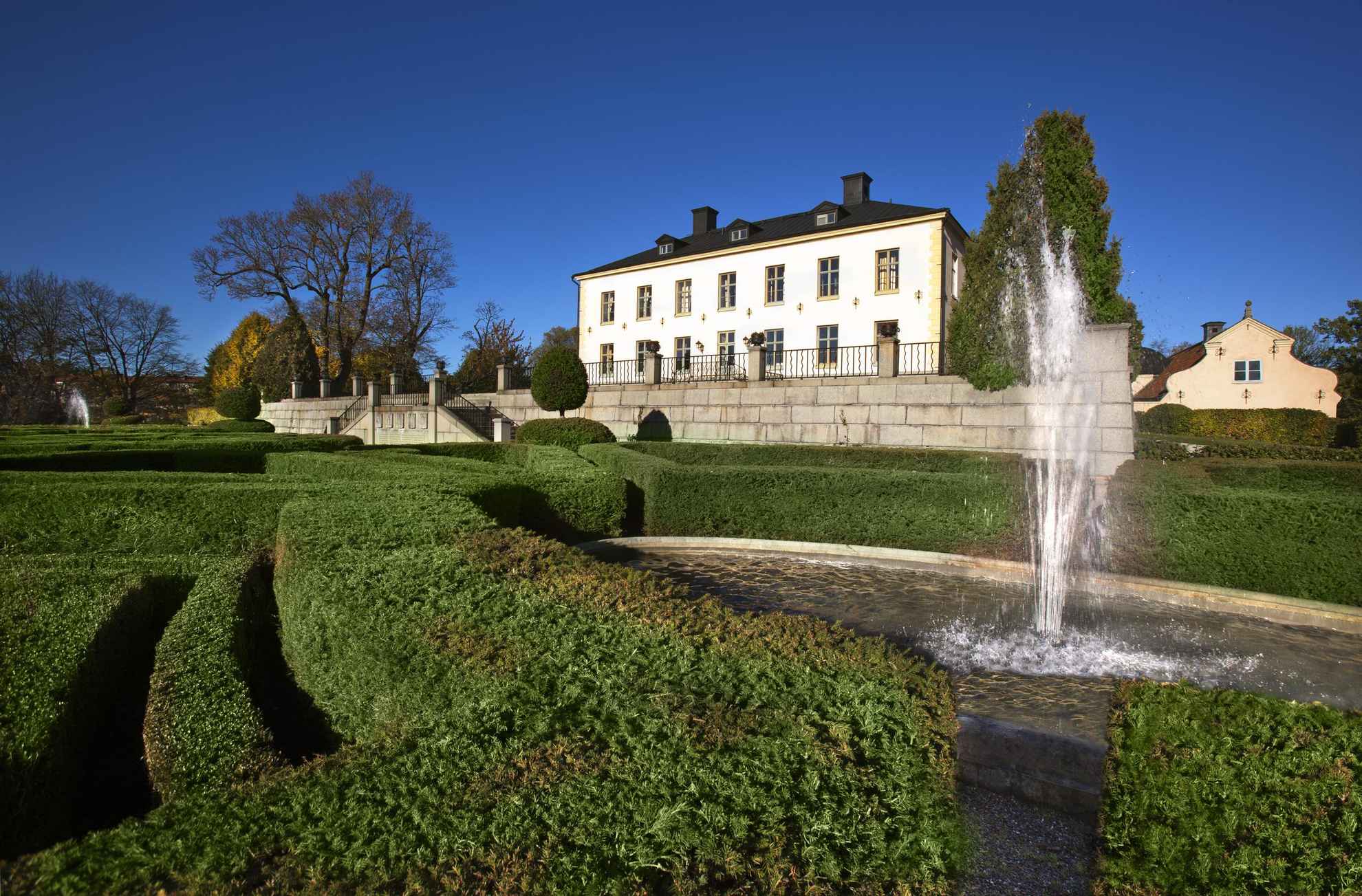 Die Fassade von Schloss Hesselby ist beige. Vom Hof führt eine Treppe hinunter in einen Garten mit einem Springbrunnen.