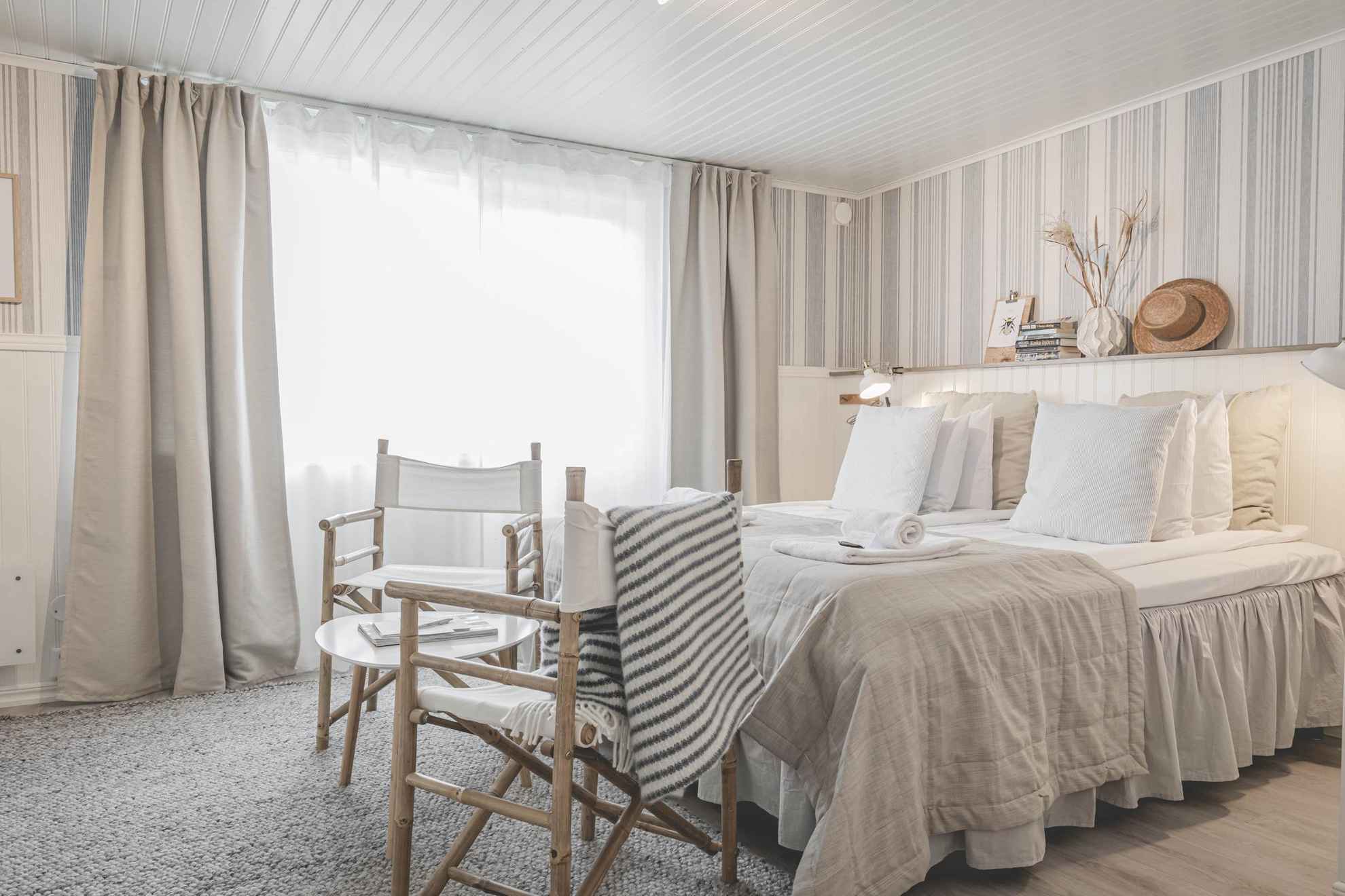 Ein Hotelzimmer in StrandNära. Das Zimmer hat ein großes Bett, einen kleinen Tisch und zwei Stühle. Das Zimmer ist in Weiß und Beige gehalten.