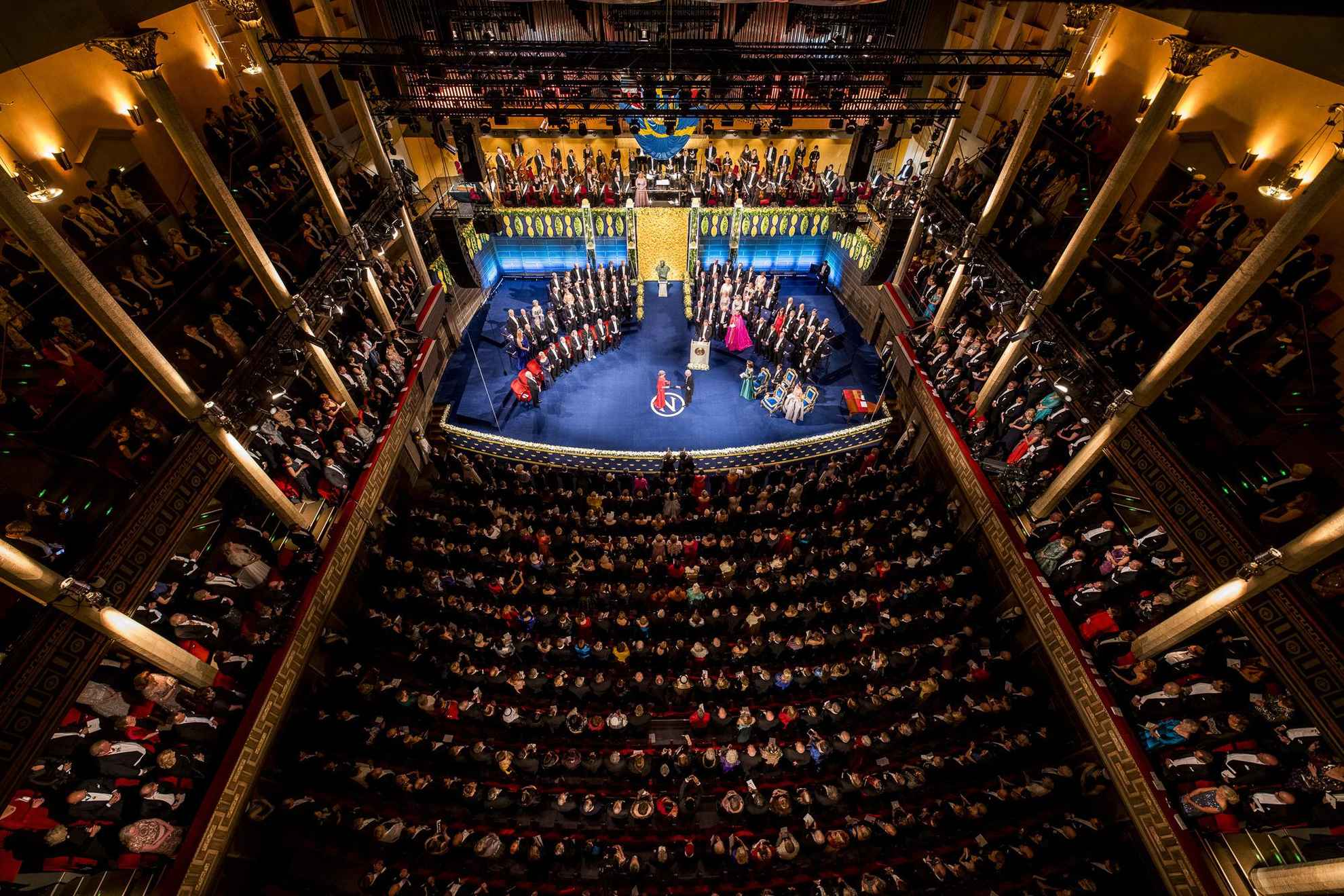 Ein Saal voller Menschen, die auf die Bühne schauen, auf der die Preisträger ihren Nobelpreis erhalten.