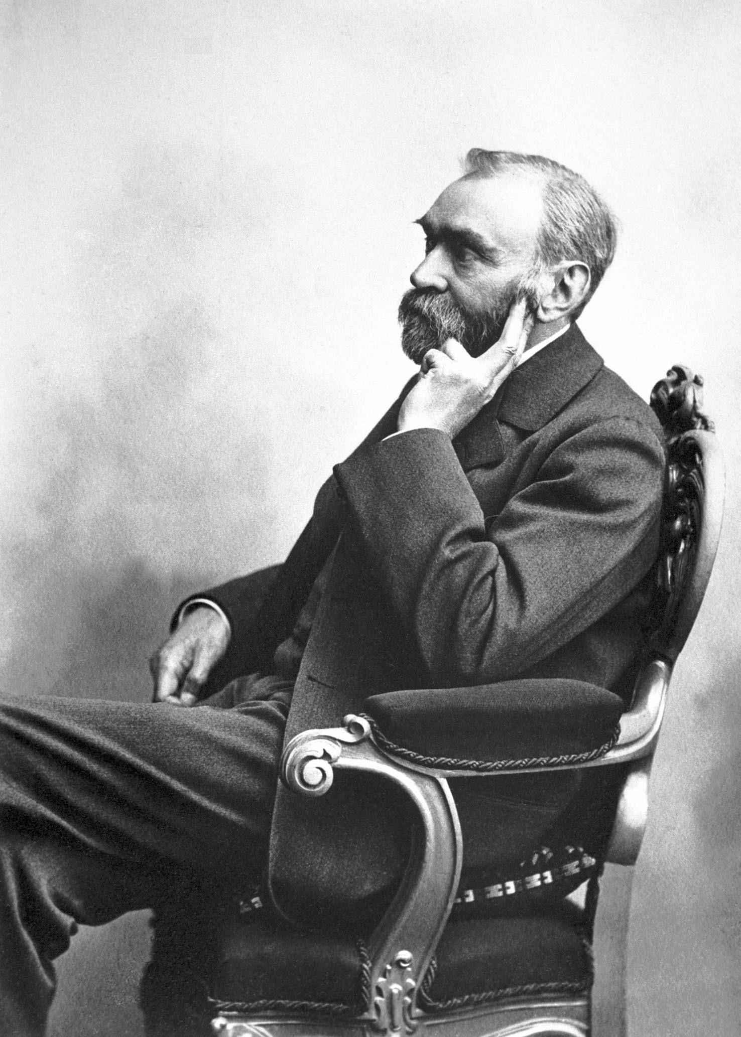 Ein altes Schwarz-Weiß-Porträt von Alfred Nobel, auf einem Stuhl sitzend.