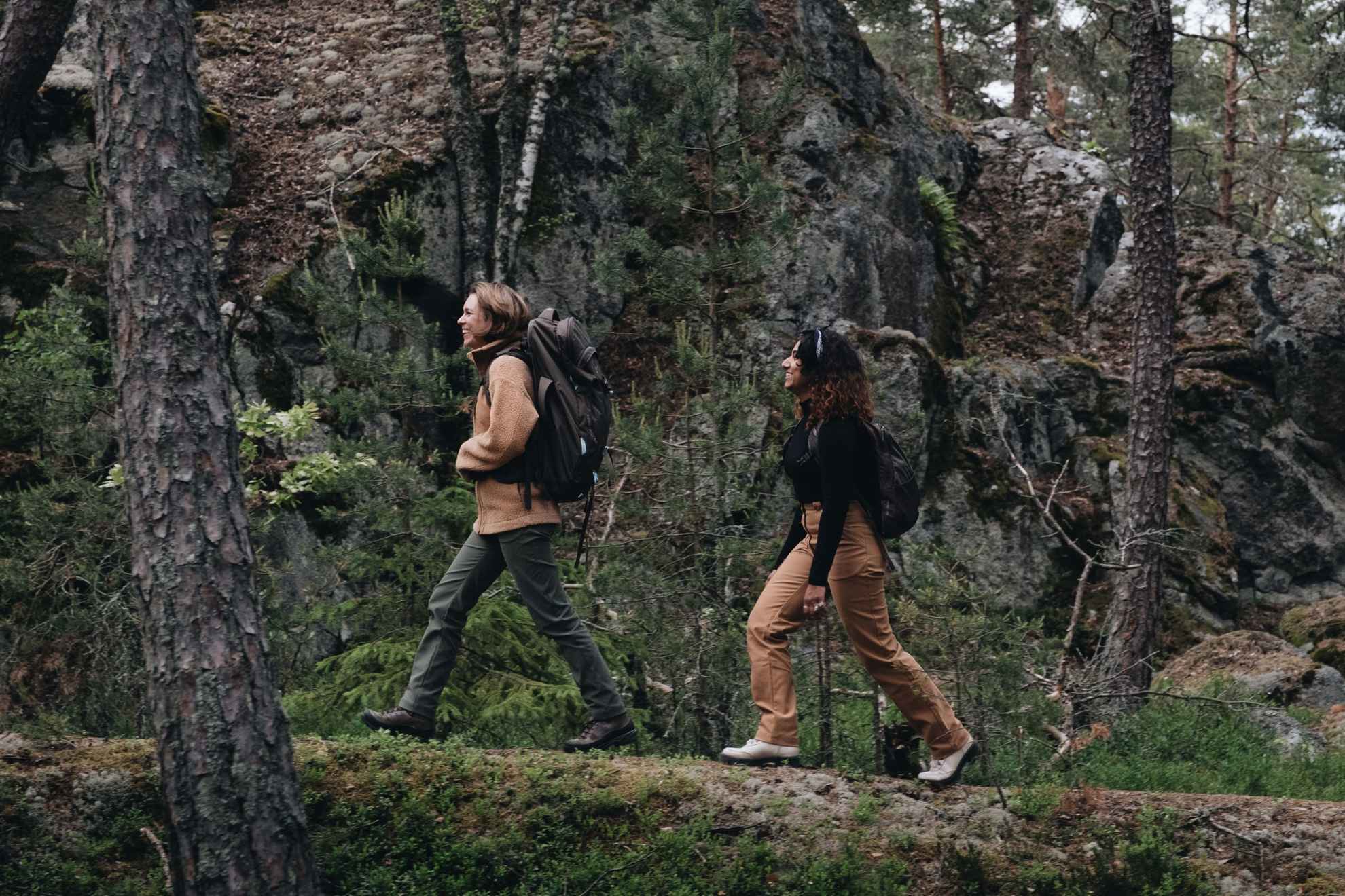 Zwei Frauen in Outdoor-Kleidung wandern in einem Wald.
