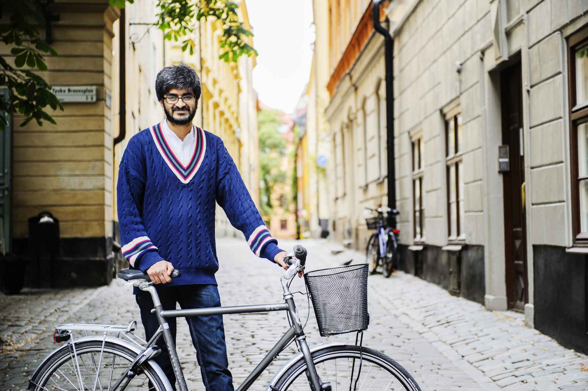 A man with a beard and glasses is standing next to his bike on one of the cobbled streets in the Old Town of Stockholm.