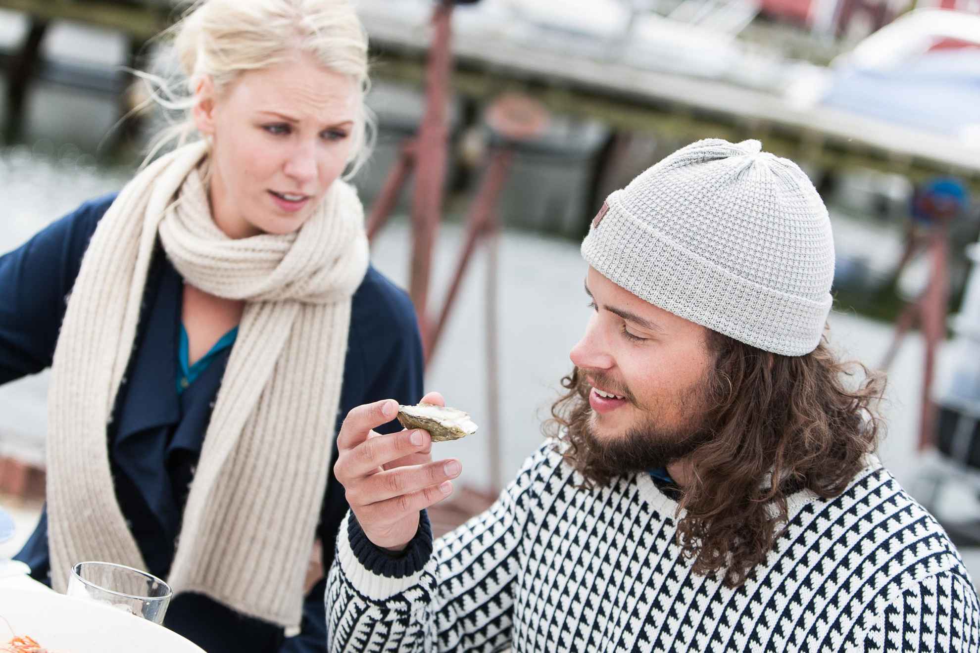 Ein Mann und eine Frau sitzen an einem Tisch im Freien. Der Mann hält eine Auster in der Hand.