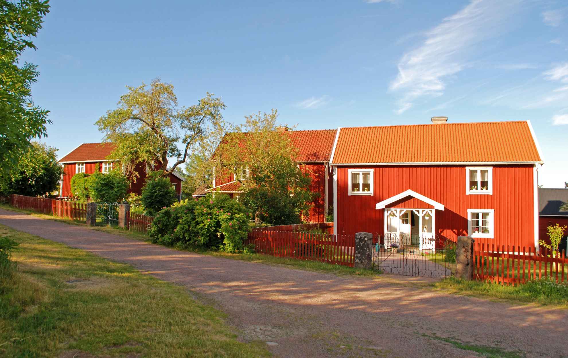 Drei rote Häuser mit weißen Ecken und ein großer Garten an einem Sommertag.