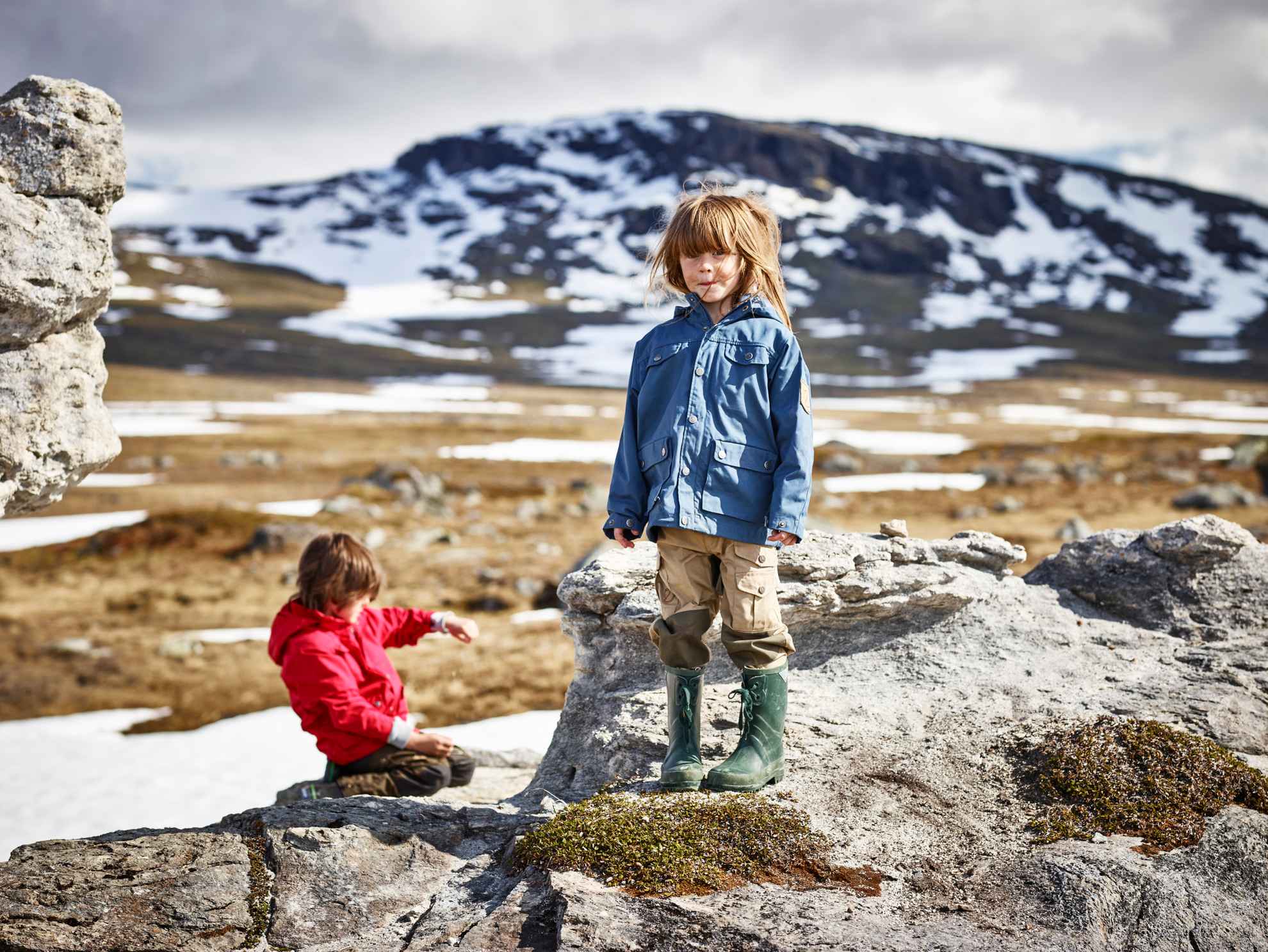 Zwei Kinder auf einer Wanderung in Padjelanta in Nordschweden, umgeben von Schneeflecken und Berggipfeln.