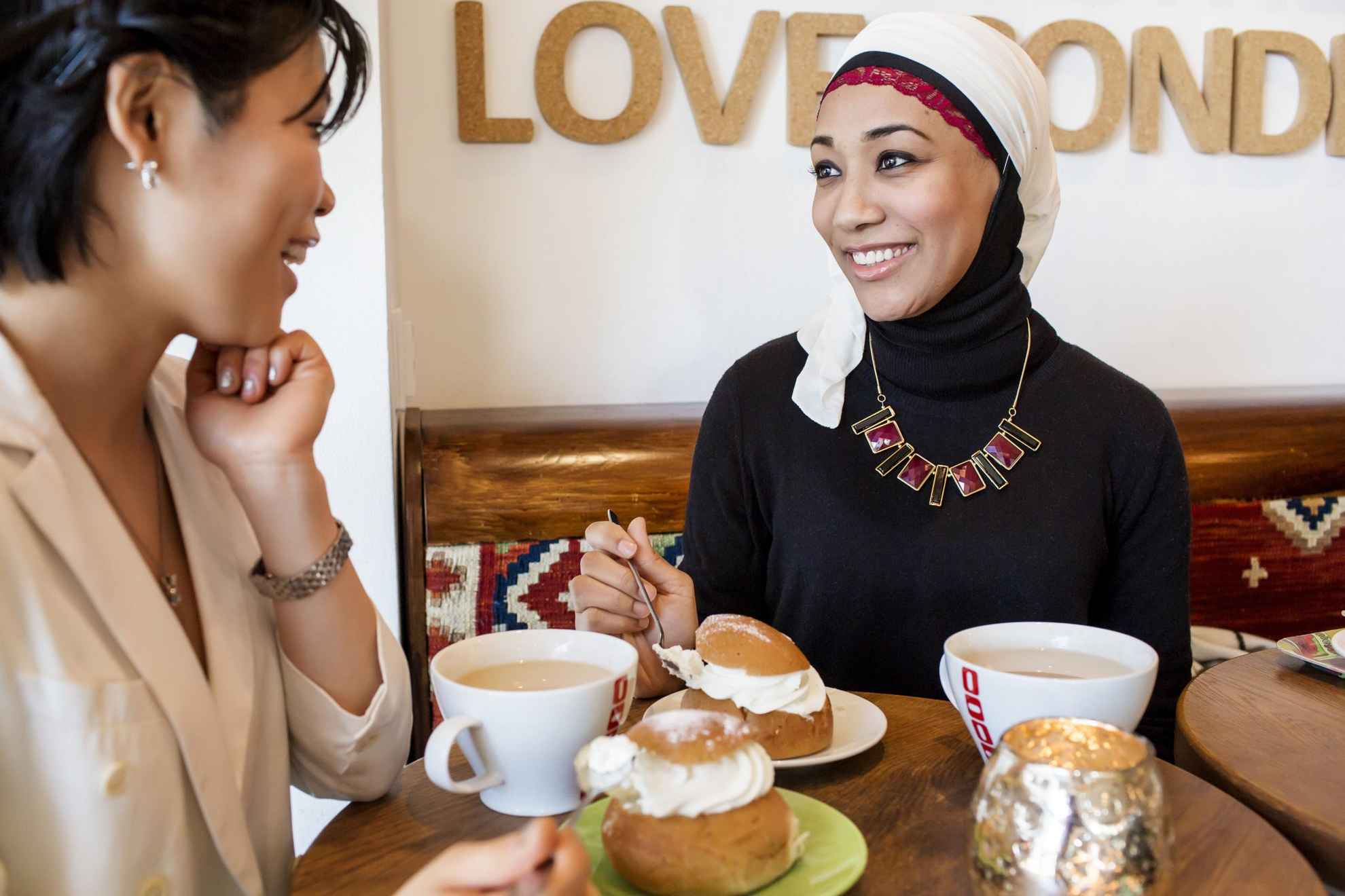 Zwei Frauen sitzen in einem schwedischen Café, trinken Kaffee und essen ein schwedisches Sahnebrötchen namens Semla.