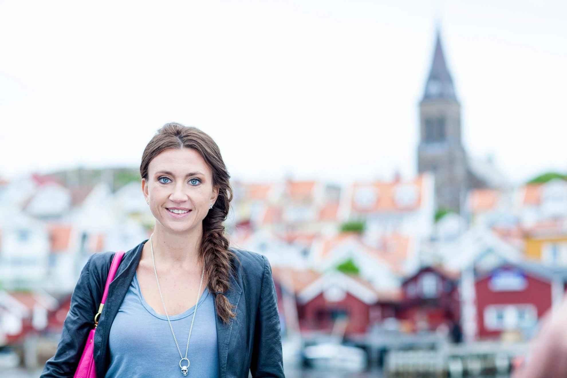 Autorin Camilla Läckberg steht vor Bootshäusern und einer Kirche in der Ferne.