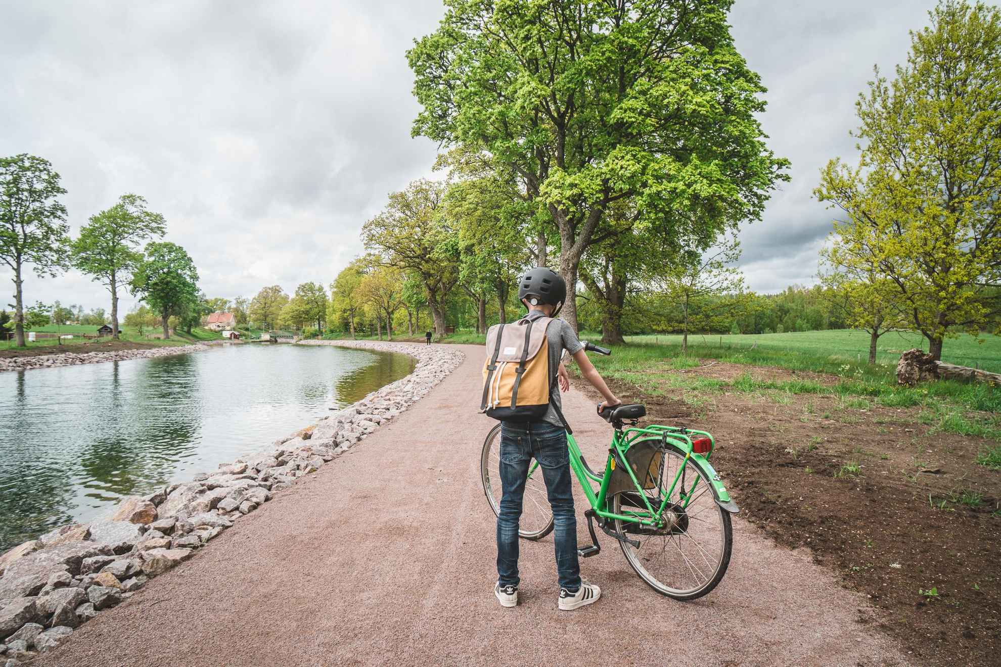 Ein Junge, der neben seinem grünen Fahrrad auf einer Straße neben dem Wasser des Göta-Kanals steht.