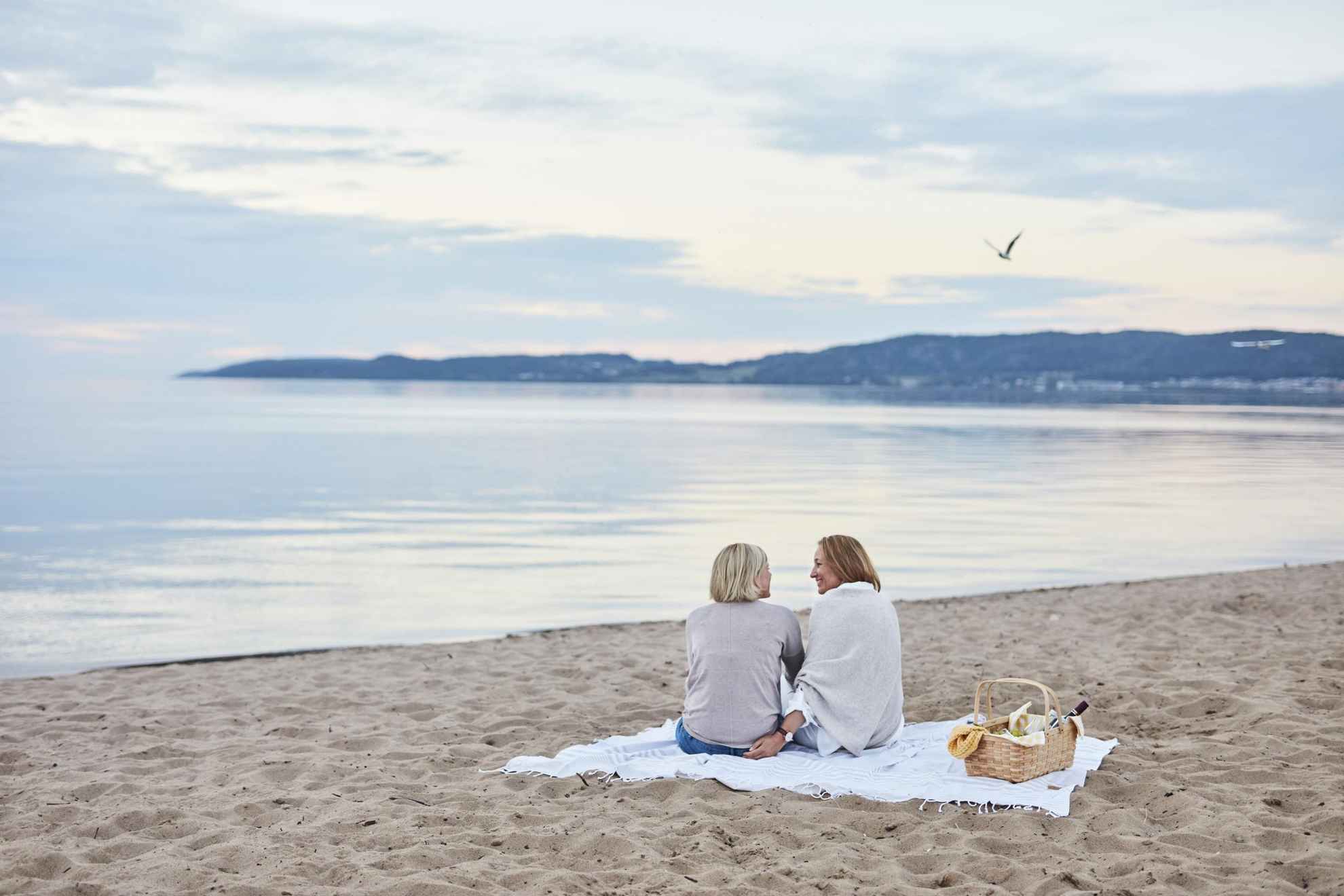 Zwei Frauen sitzen auf einer Decke am Strand.