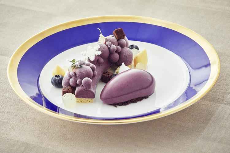 Ein lila Dessert mit Garnitur auf einem Teller in Weiß und Blau mit goldenem Rand.