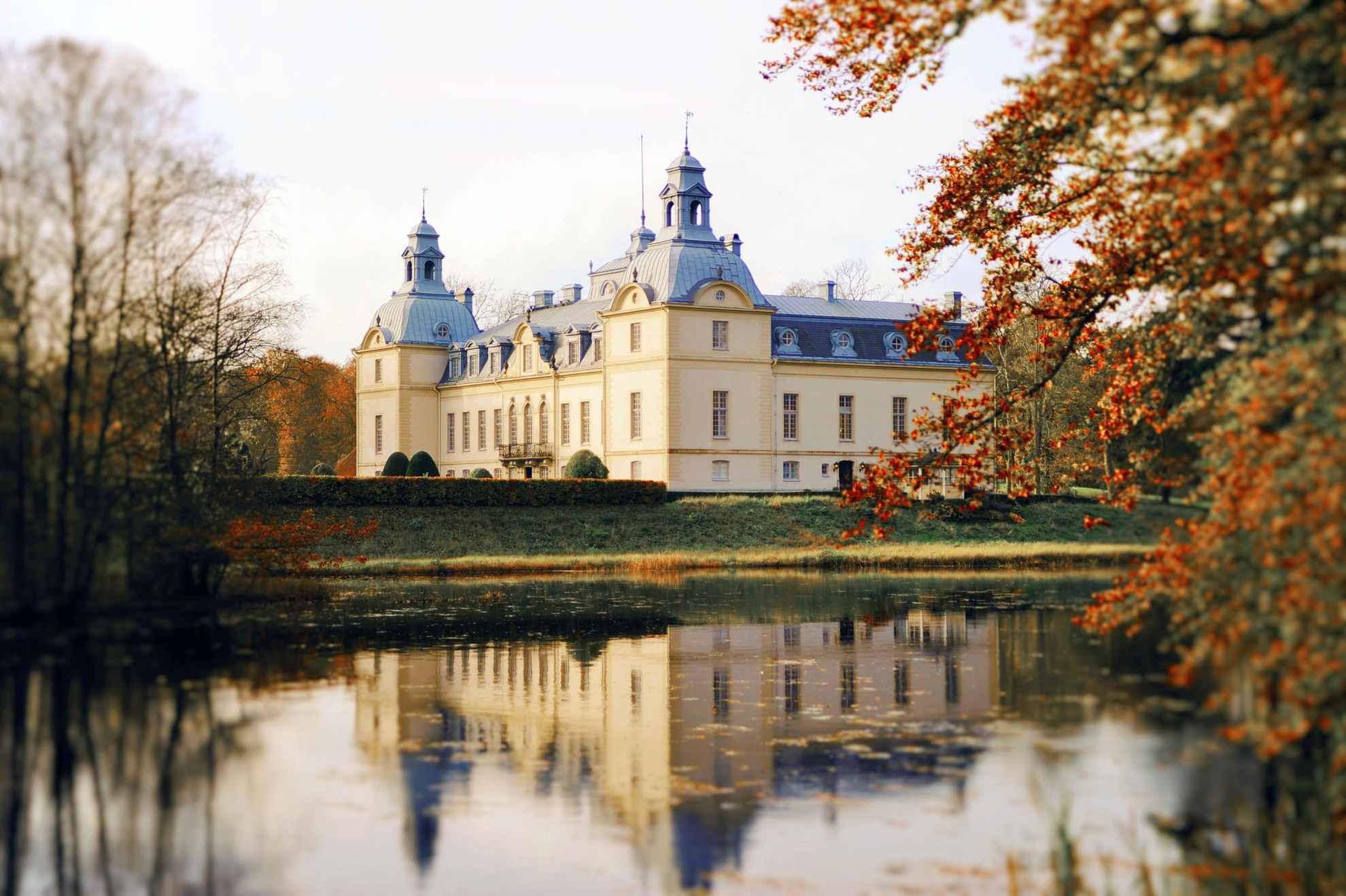 Schloss Kronovall an einem See im Herbst. Das Schloss spiegelt sich im Wasser.