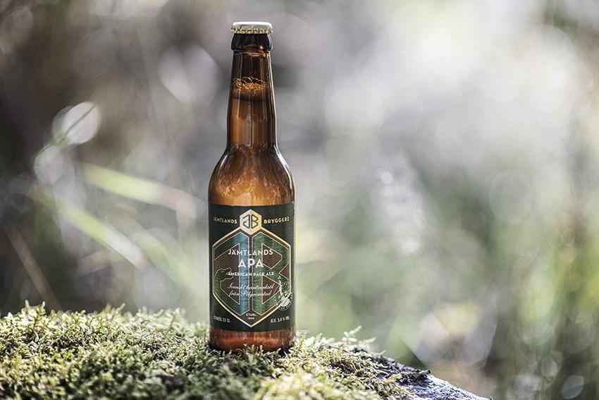 Eine Glasflasche Bier steht in der  Natur auf Moos.