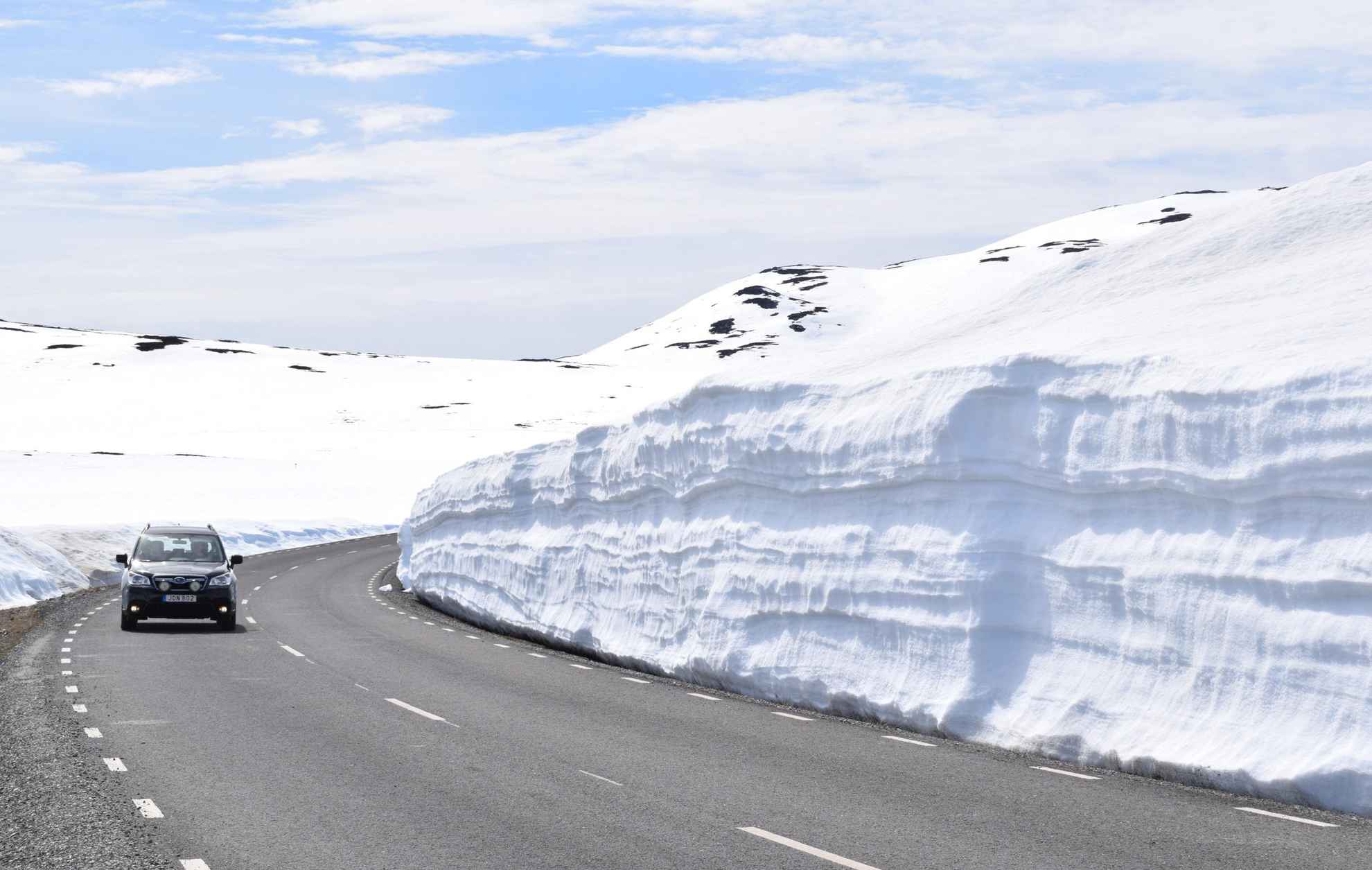 Ein Auto fährt auf einer Straße, die von hohen Schneewällen umgeben ist.