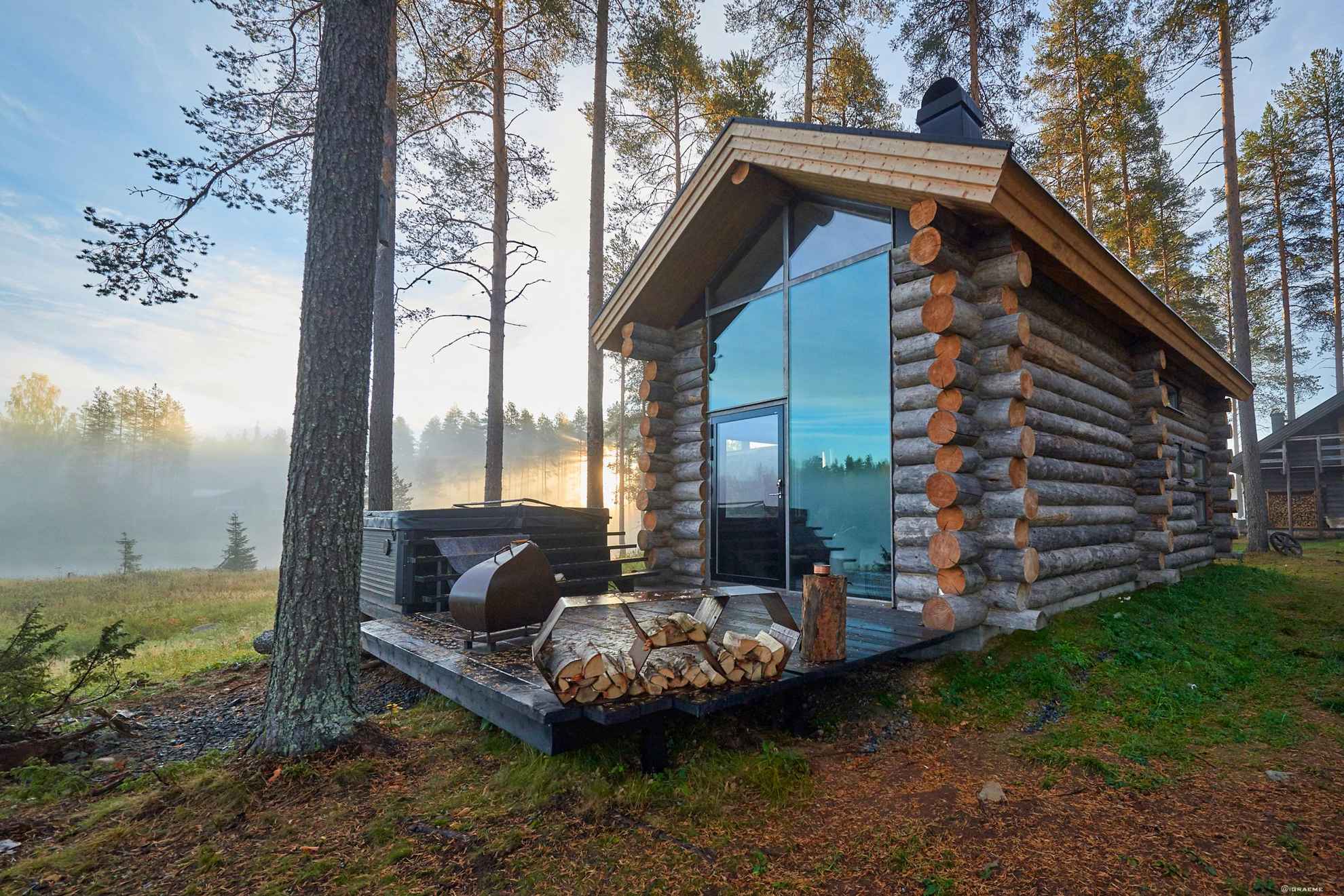Eine Blockhütte im Arctic Retreat in Schwedisch Lappland steht zwischen Bäumen. Die Natur spiegelt sicht in der Fensterfasade der Blockhütte.