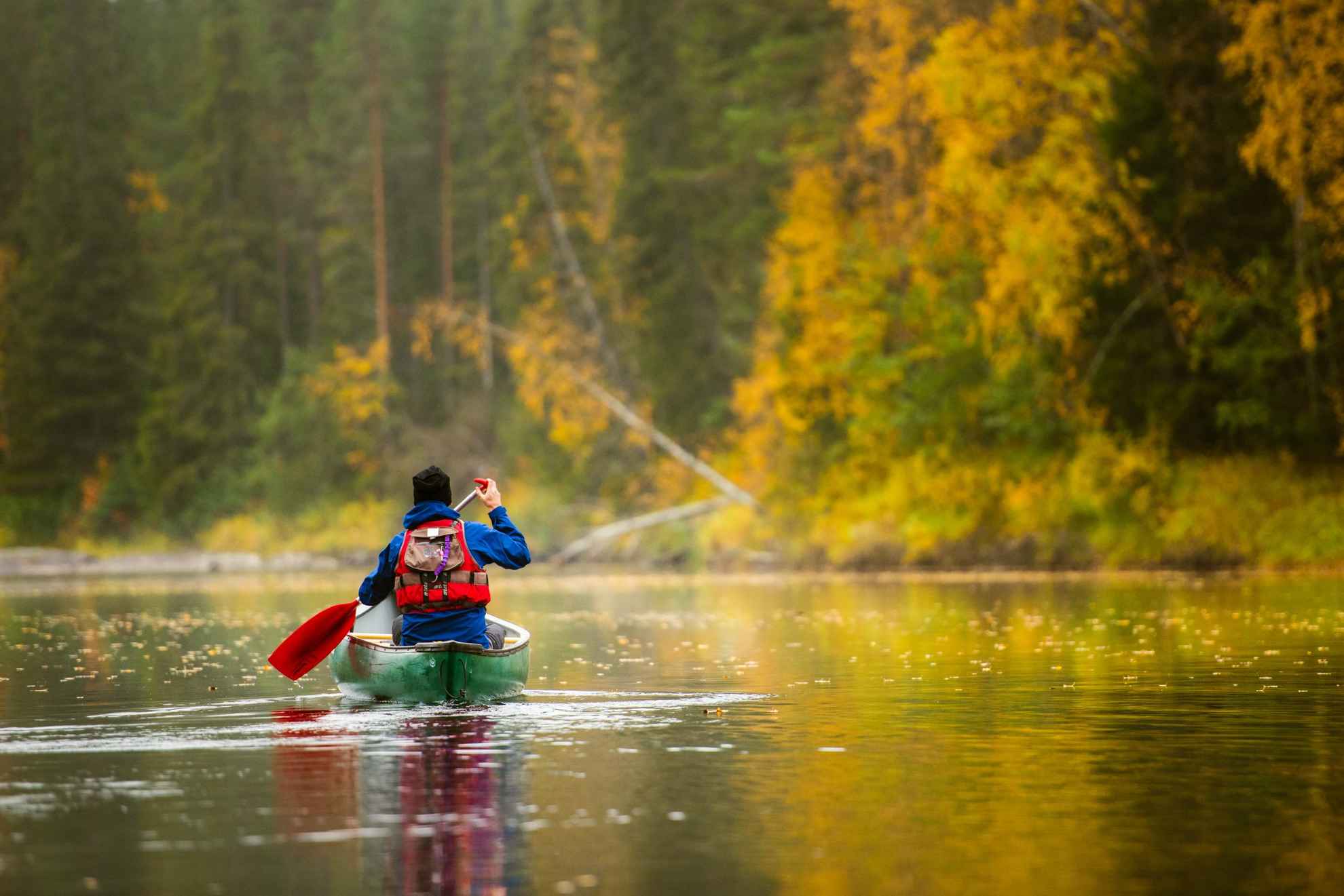 Eine Person fährt Kanu auf dem Fluss Byske während eines Herbsttages auf einem See inmitten Schwedens Natur.