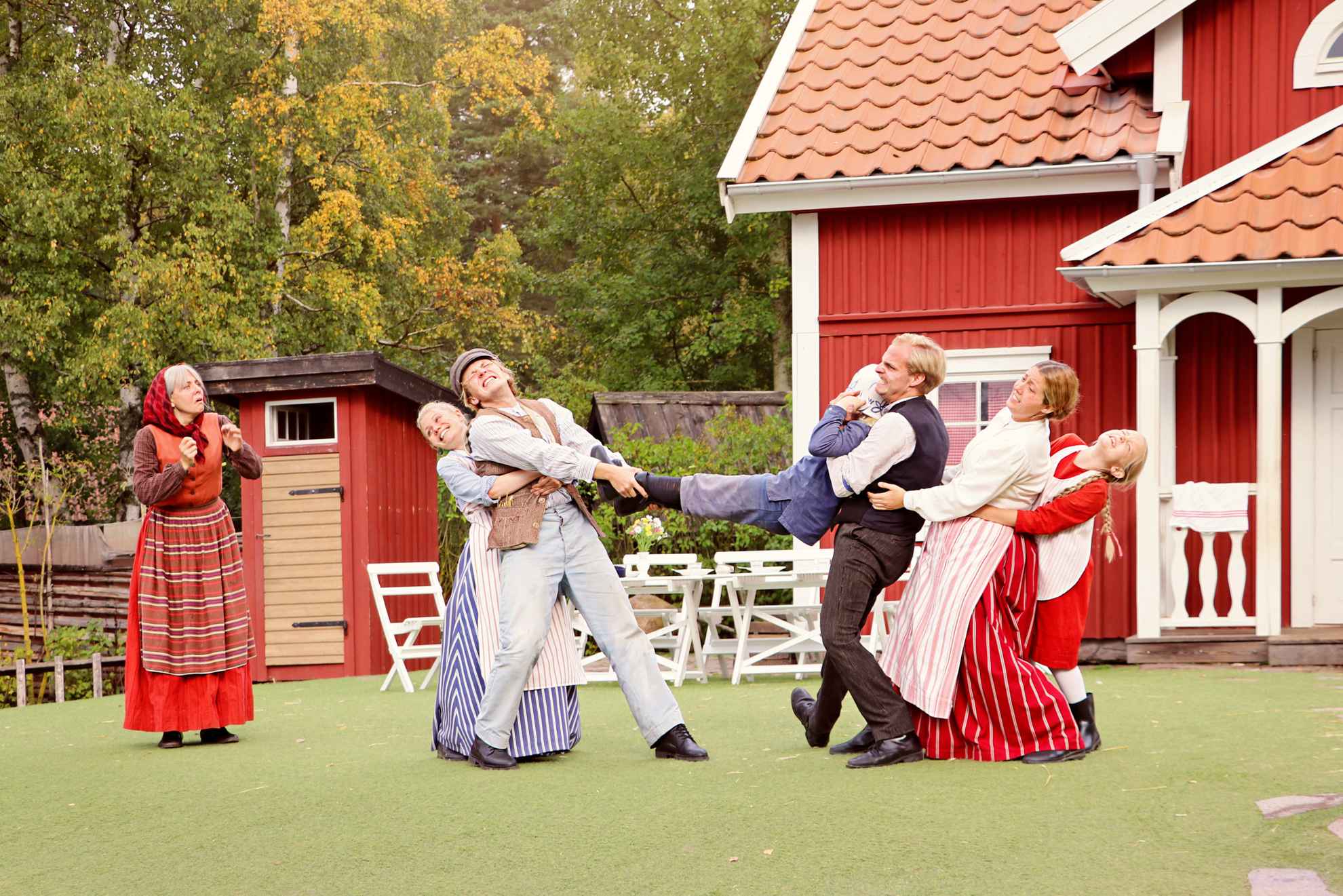 Menschen sind in 20er Jahre Outfits verkleidet und führen das Theaterstück Michel aus Lönneberga vor einer aus roten Häusern bestehenden Kulisse auf.