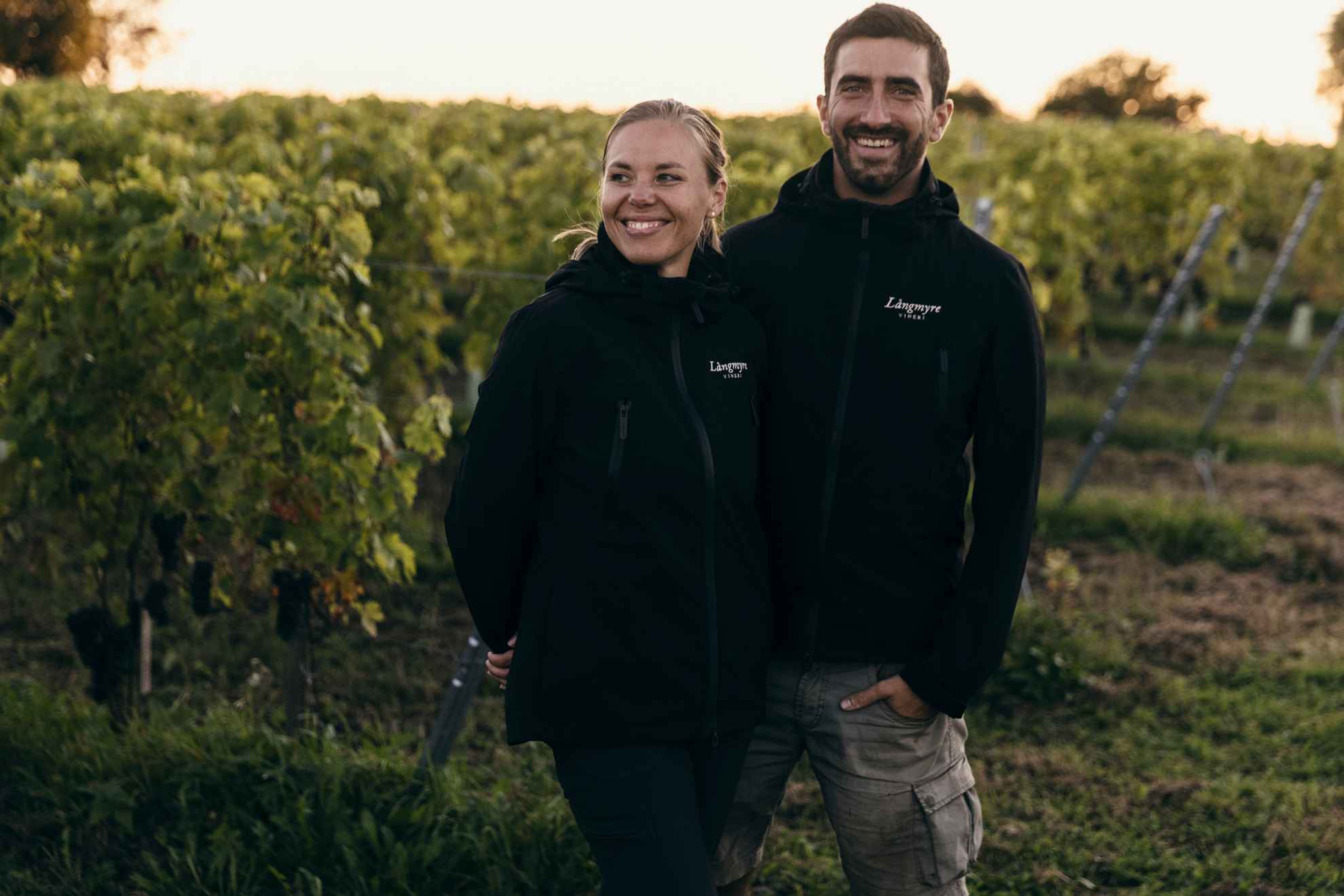 Emma Serner und Andrea Guerra stehen vor grünen Weinstöcken auf ihrem Weinberg in Långmyre.