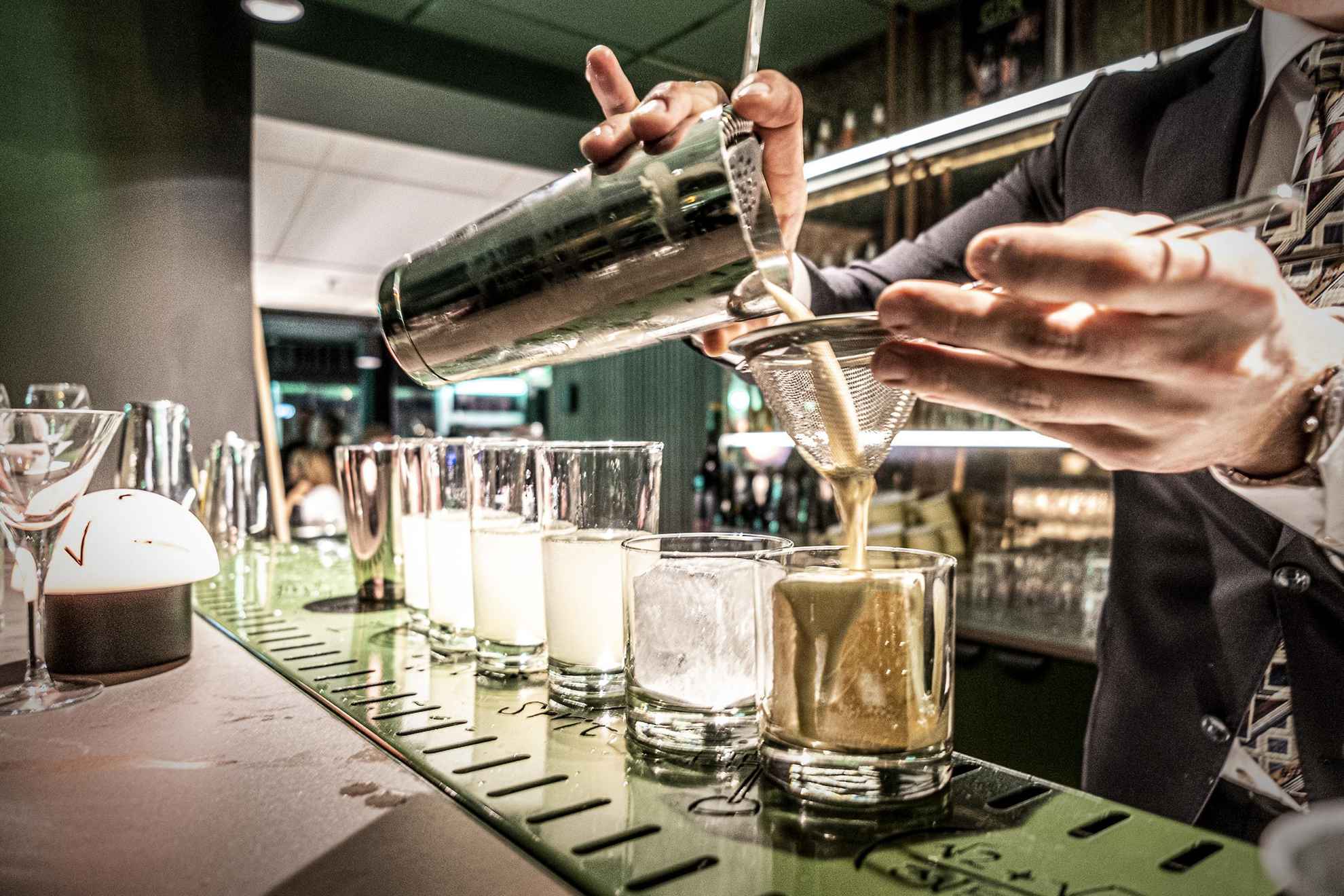 Ein Barkeeper gießt einen Cocktail aus dem Shaker in ein Glas.