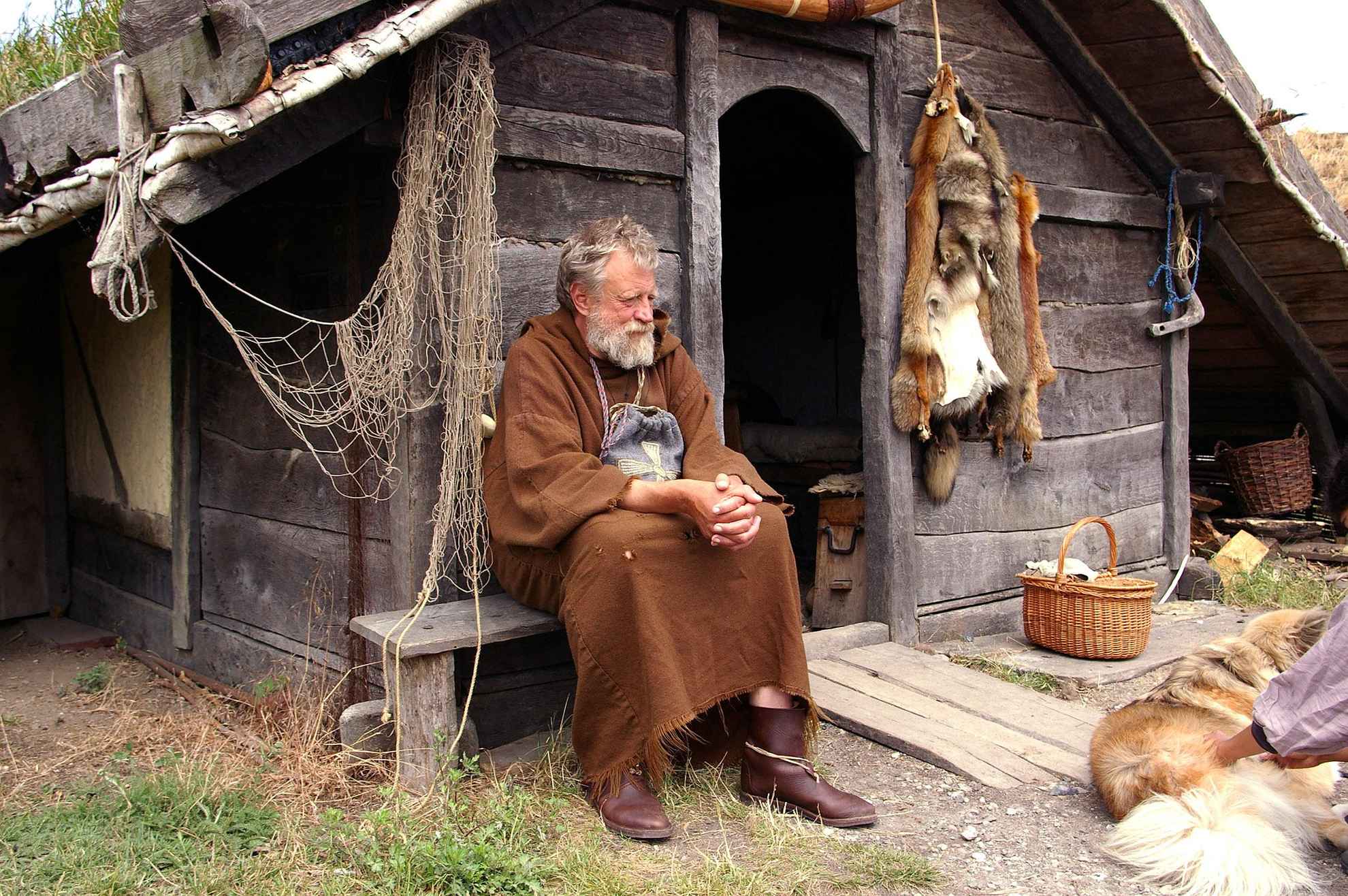 Ein alter Mann, der als Wikinger verkleidet ist, sitzt vor einem alten Holzhaus.