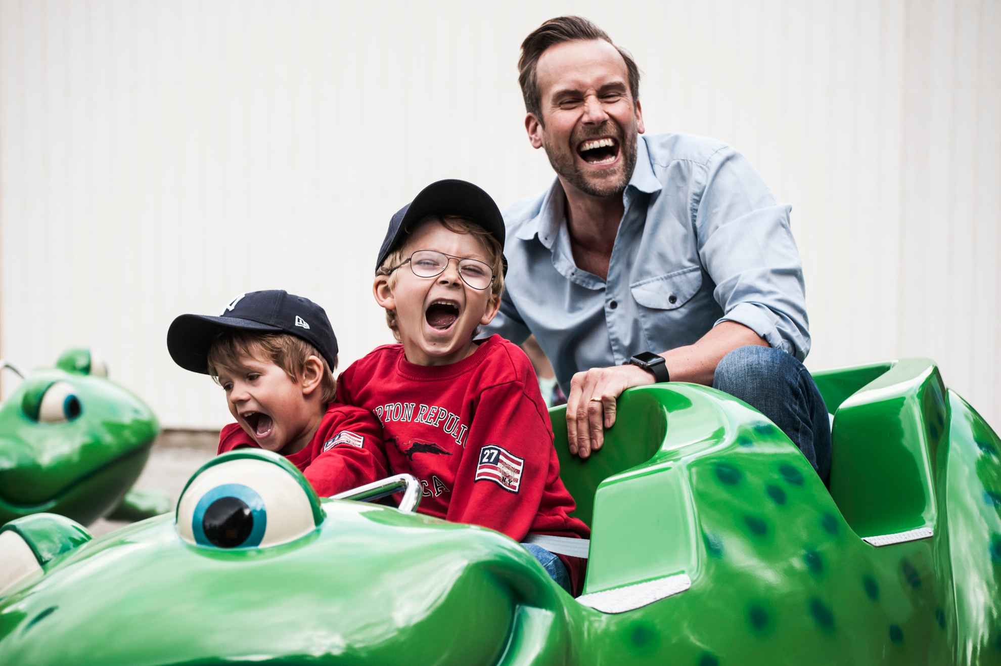 Two laughing boys in comapny with a man riding a green roller coaster at Furuvik