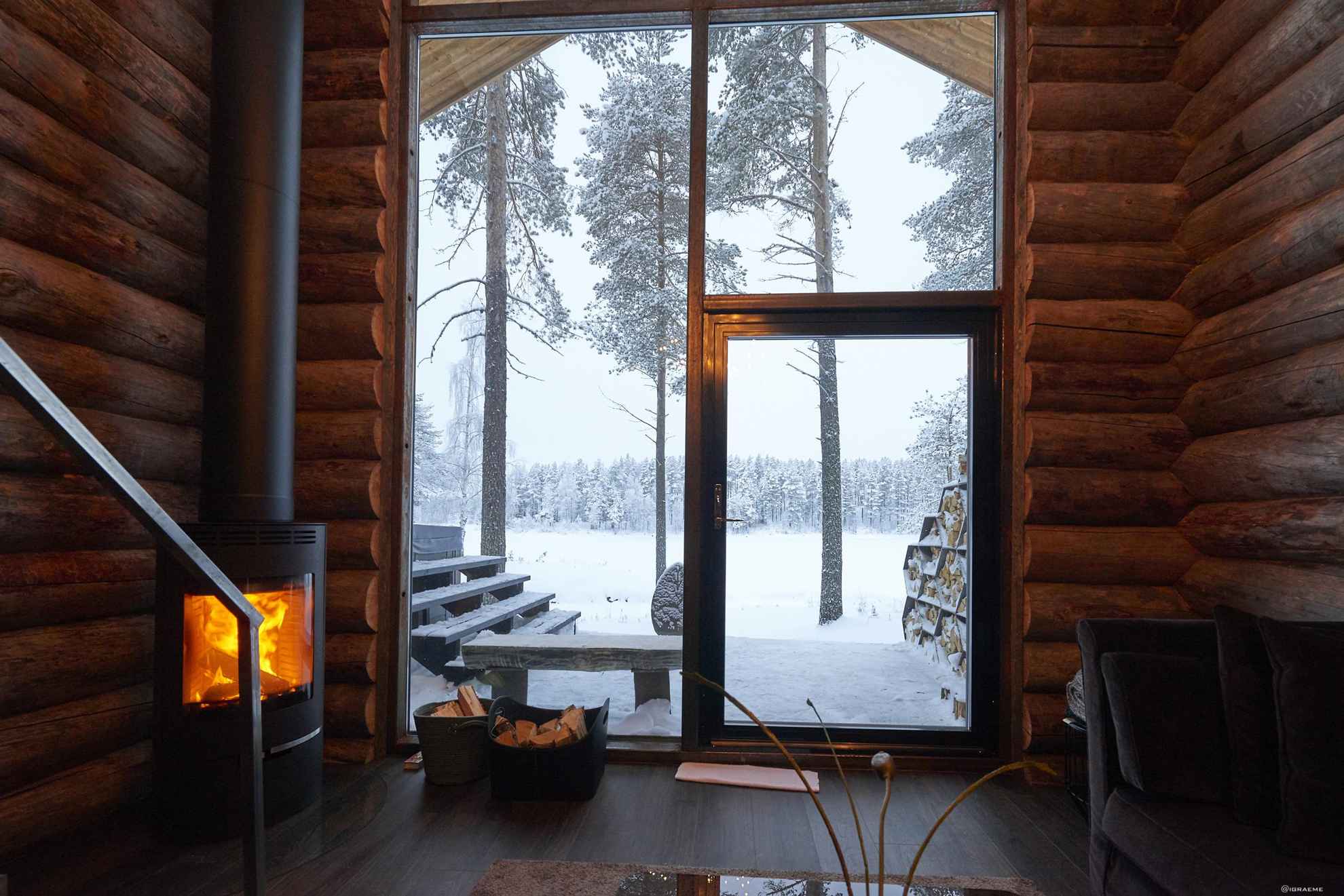 Ein Holzblockhaus mit Kamin und großen Fenstern. Winter im Arctic Retreat in Schwedisch Lappland