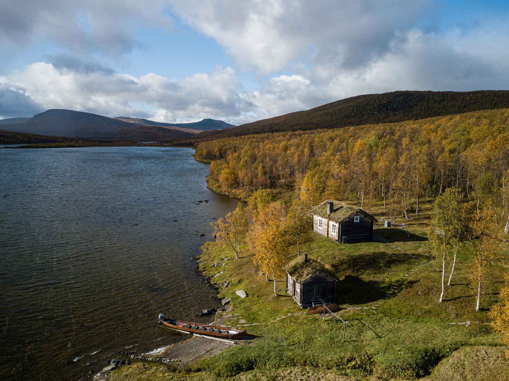 Luftaufnahme einer Küstenlandschaft zeigt die Häuser der  Geunja Die Sámi Eco Lodge liegt an einem See in Schwedisch Lappland