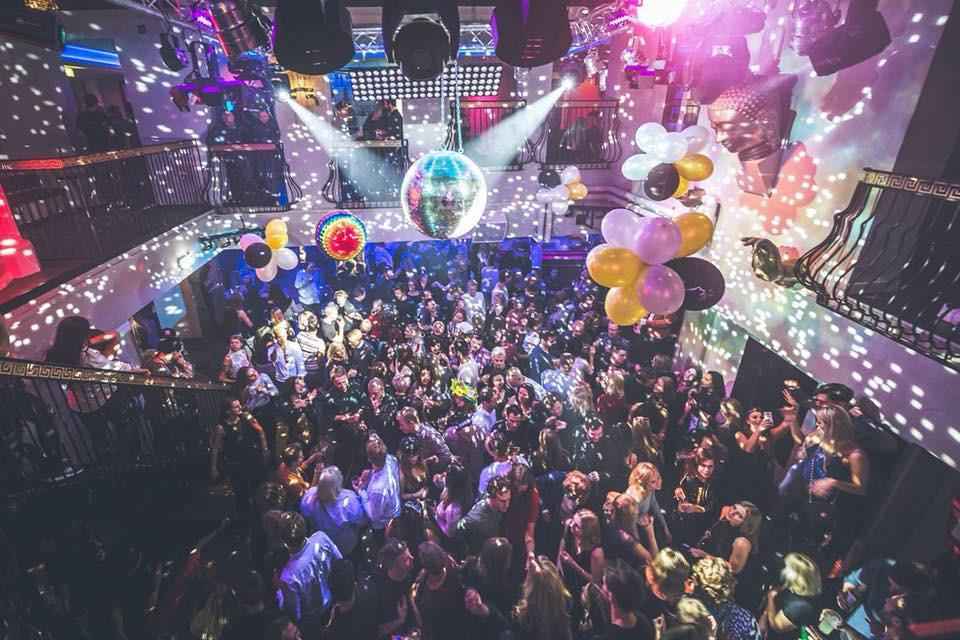Menschen tanzen in einem Nachtclub. Von der Decke hängen Luftballons und Dekoration.