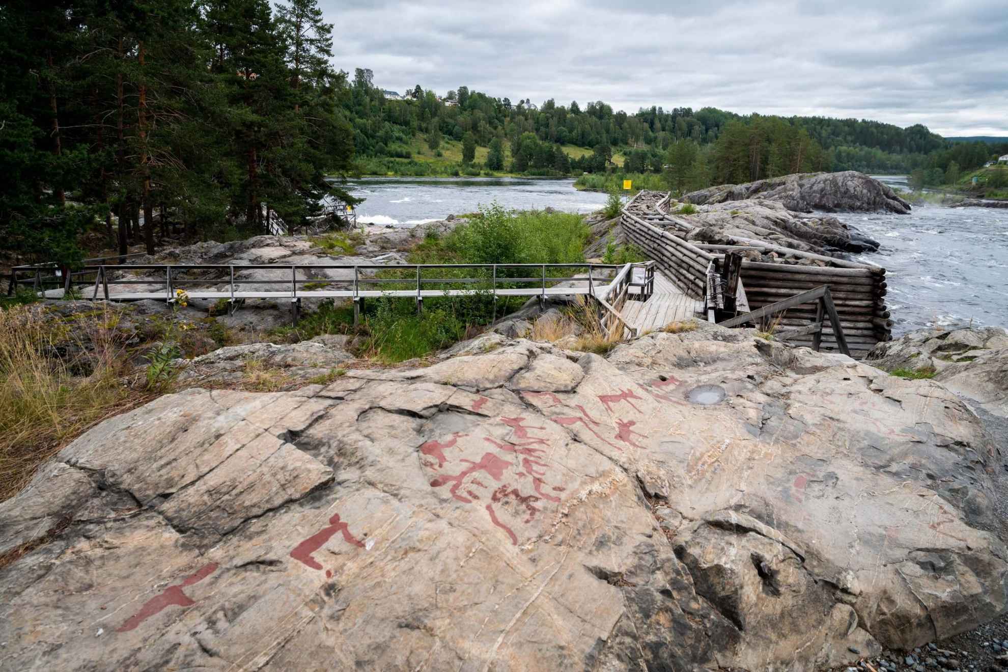 Rot ausgemalte Felszeichnungen auf einer Klippe neben einem Fluss.