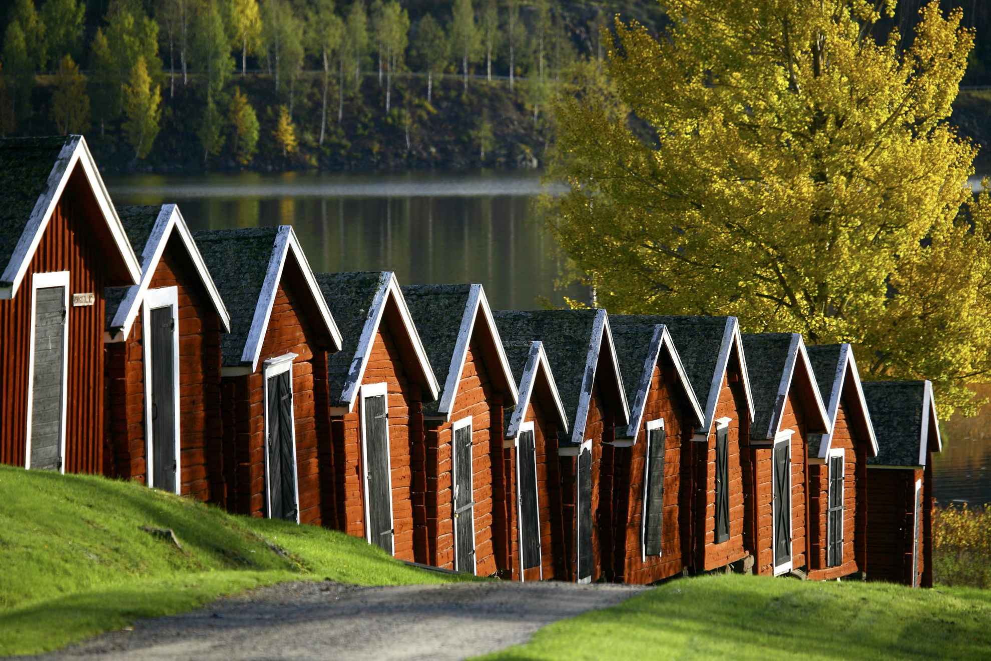 Kleine rote Holzschuppen mit schwarzen Holztüren stehen in einer Reihe dicht beieinander neben dem Wasser.