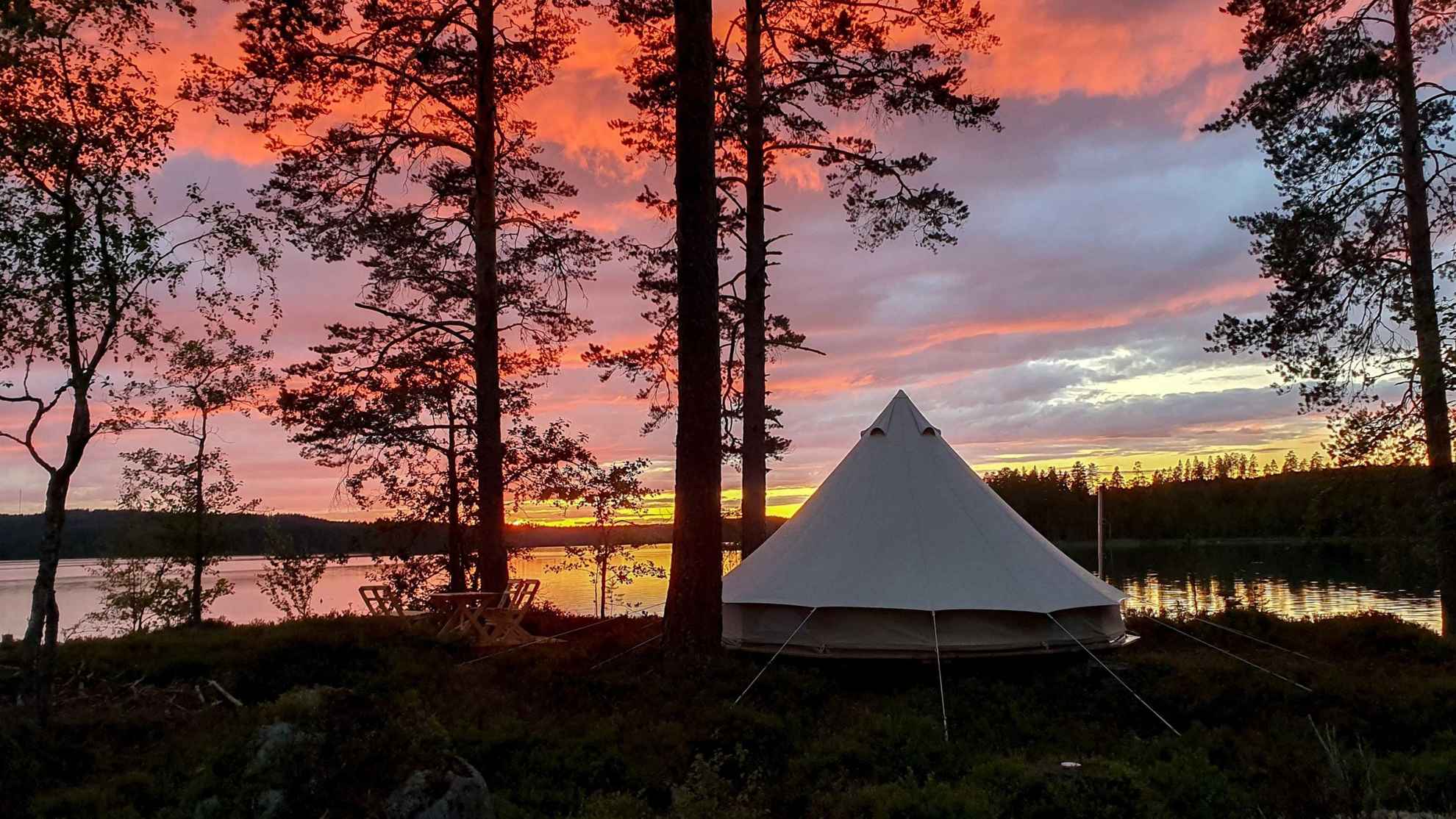 Ein Zelt steht direkt am See. Im Hintergrund ist ein imposanter Sonnenuntergang zu sehen.