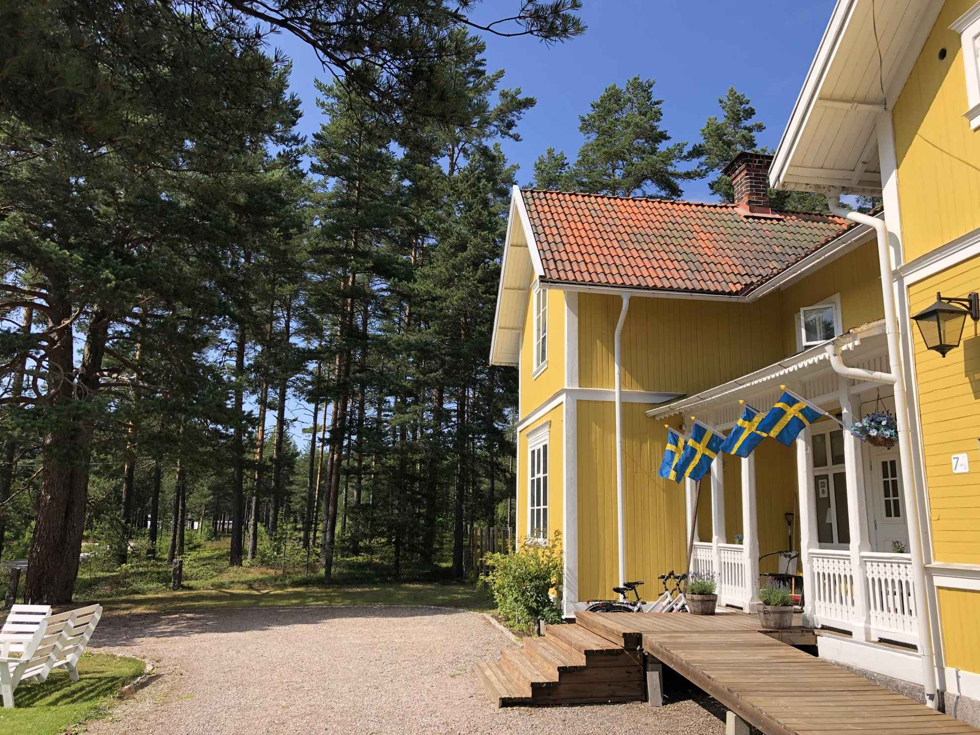 Ein gelbes Holzhaus mit vier schwedischen Flaggen, das das Äußere des Hedenstugan B&B Hotell darstellt.