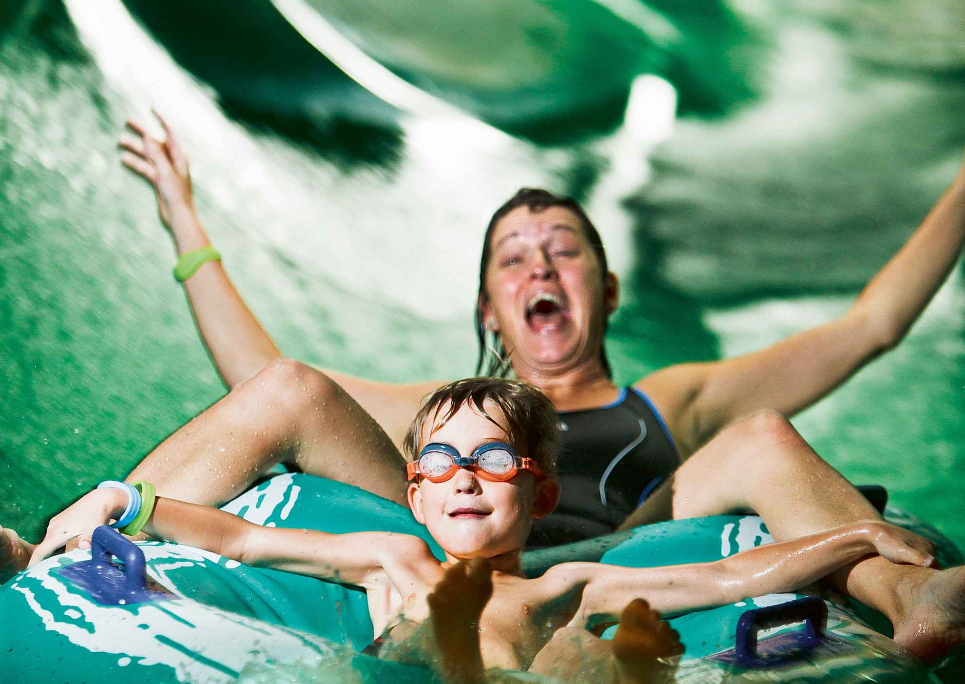 Smiling boy with swimming googles riding a tube with a laughing woman in a waterslide
