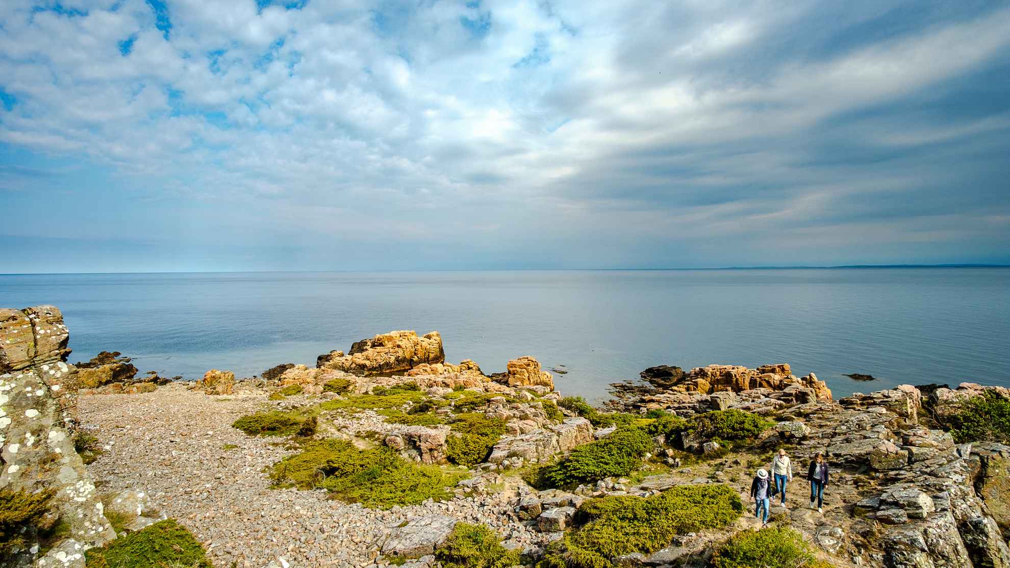 Blick auf das Meer und die Klippen im Naturschutzgebiet Hovs Hallar. Drei Menschen gehen spazieren
