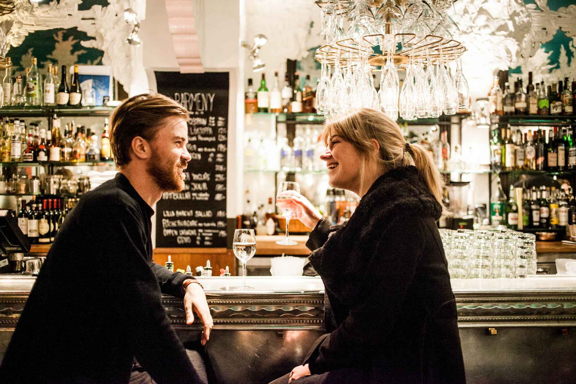Ein Mann und eine Frau sitzen in der gut beleuchteten Bar des Riche. Sie genießen ein Glas Wein an der Bar.
