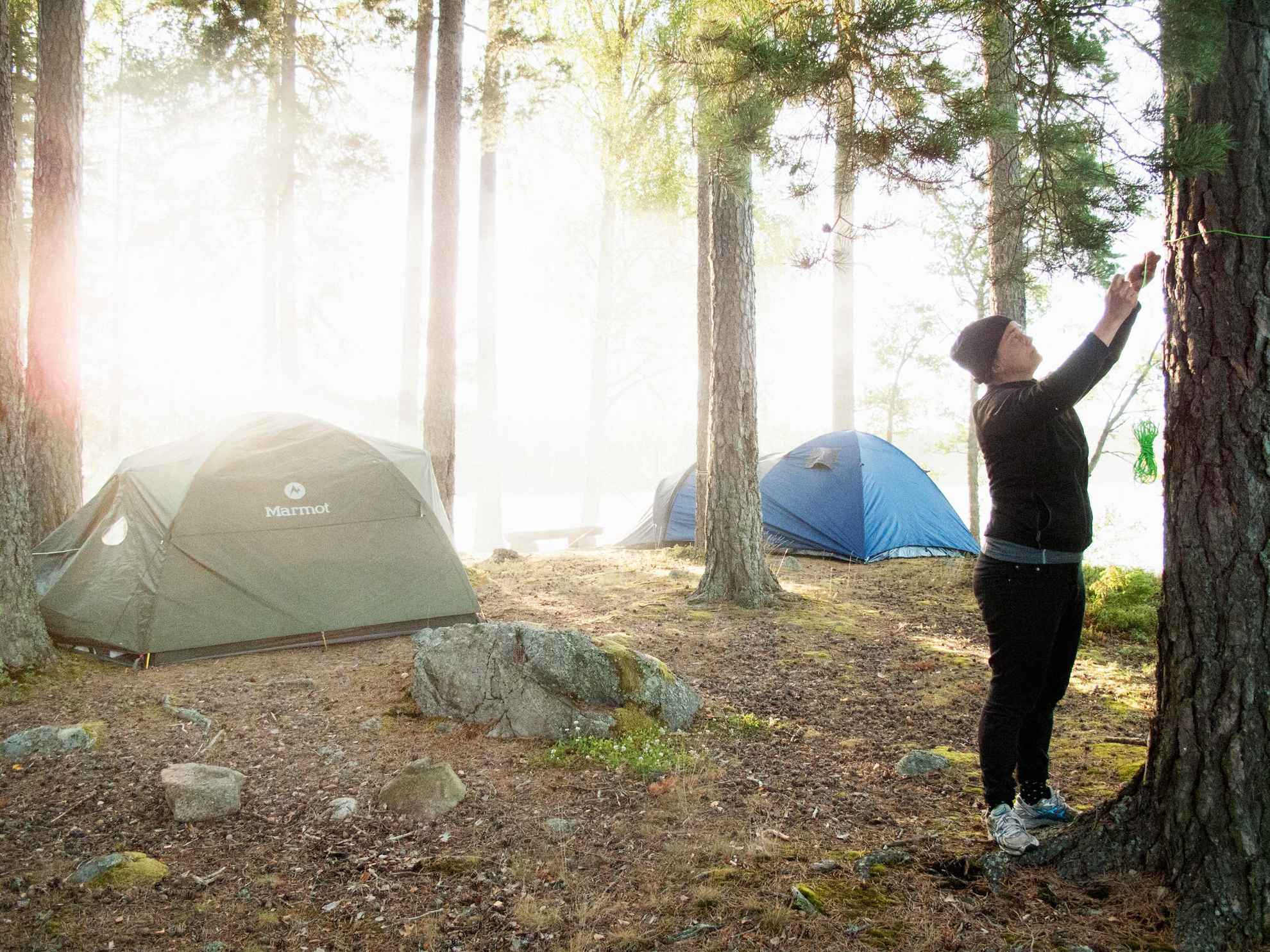 A woman is setting up a tent in the woods in Sweden.