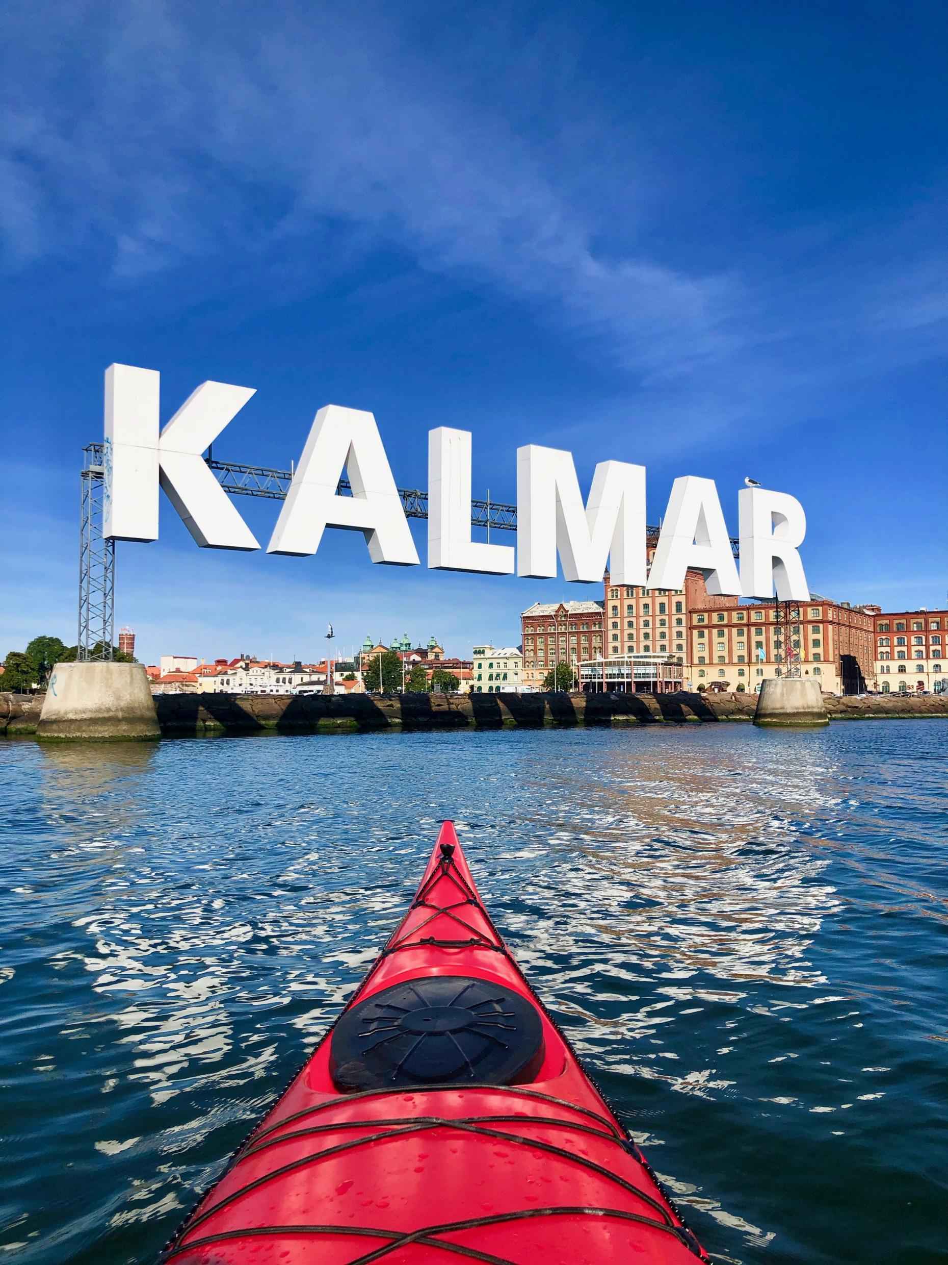 Ein großes Schild mit der Aufschrift KALMAR lädt dich in die Stadt ein. Die Vorderseite eines Kajaks auf dem Wasser auf dem Weg ins Zentrum.