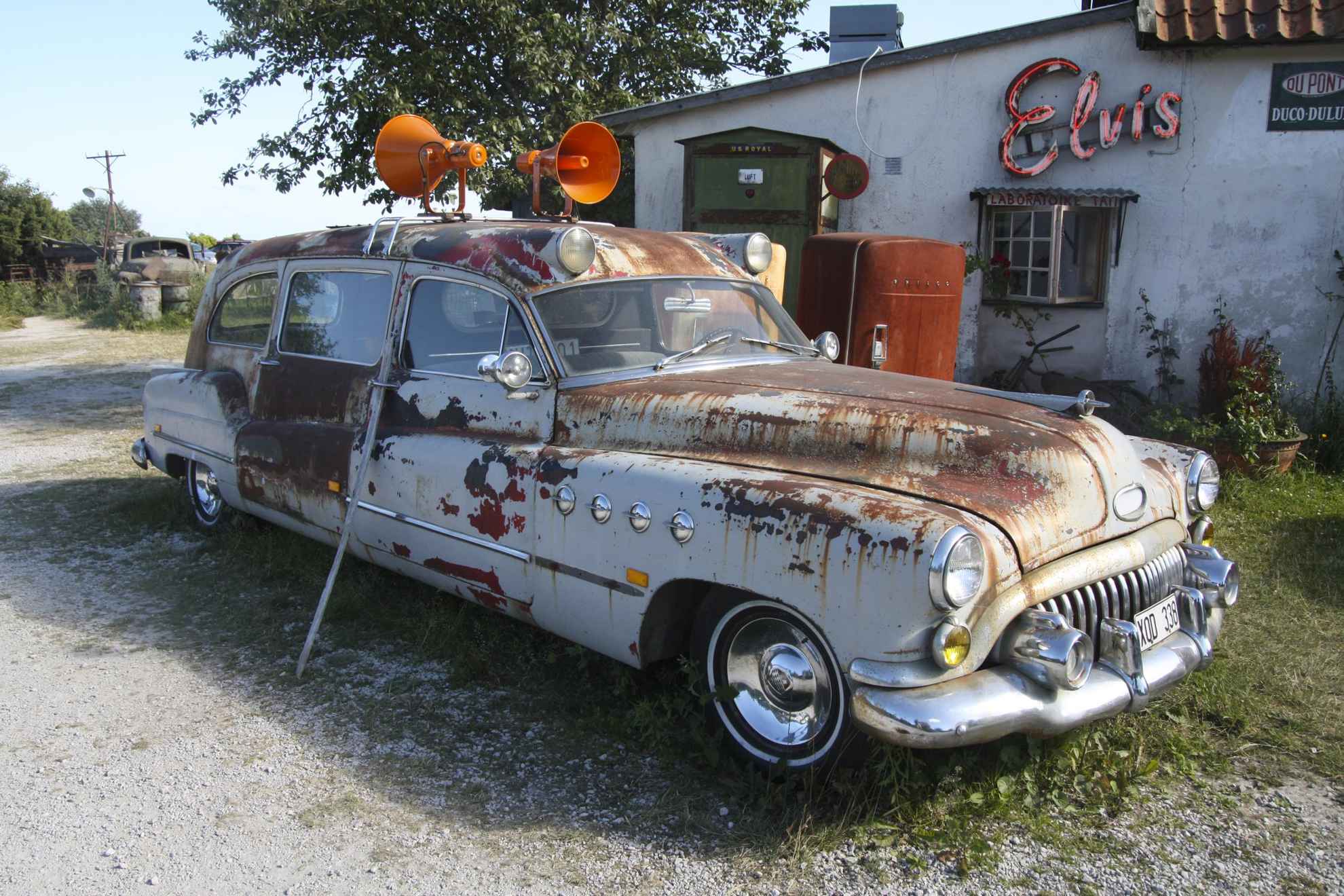 Ein altes rostiges Auto mit Sirenen auf dem Dach vor einer alten Tankstelle.