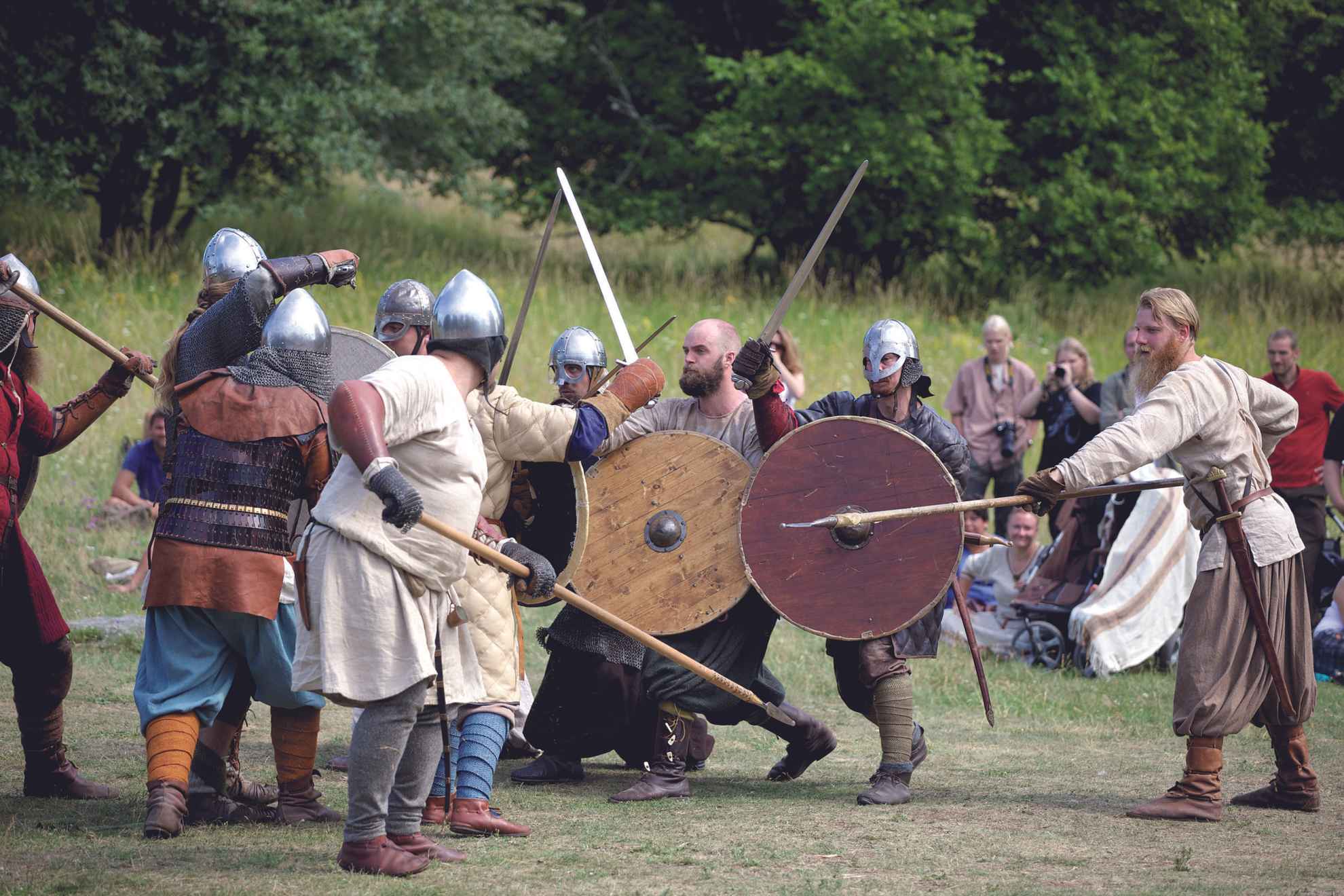 Eine Gruppe von Menschen, alle in Wikingerkleidung, spielt einen Kampf mit Speeren, Schwertern und Schilden nach.