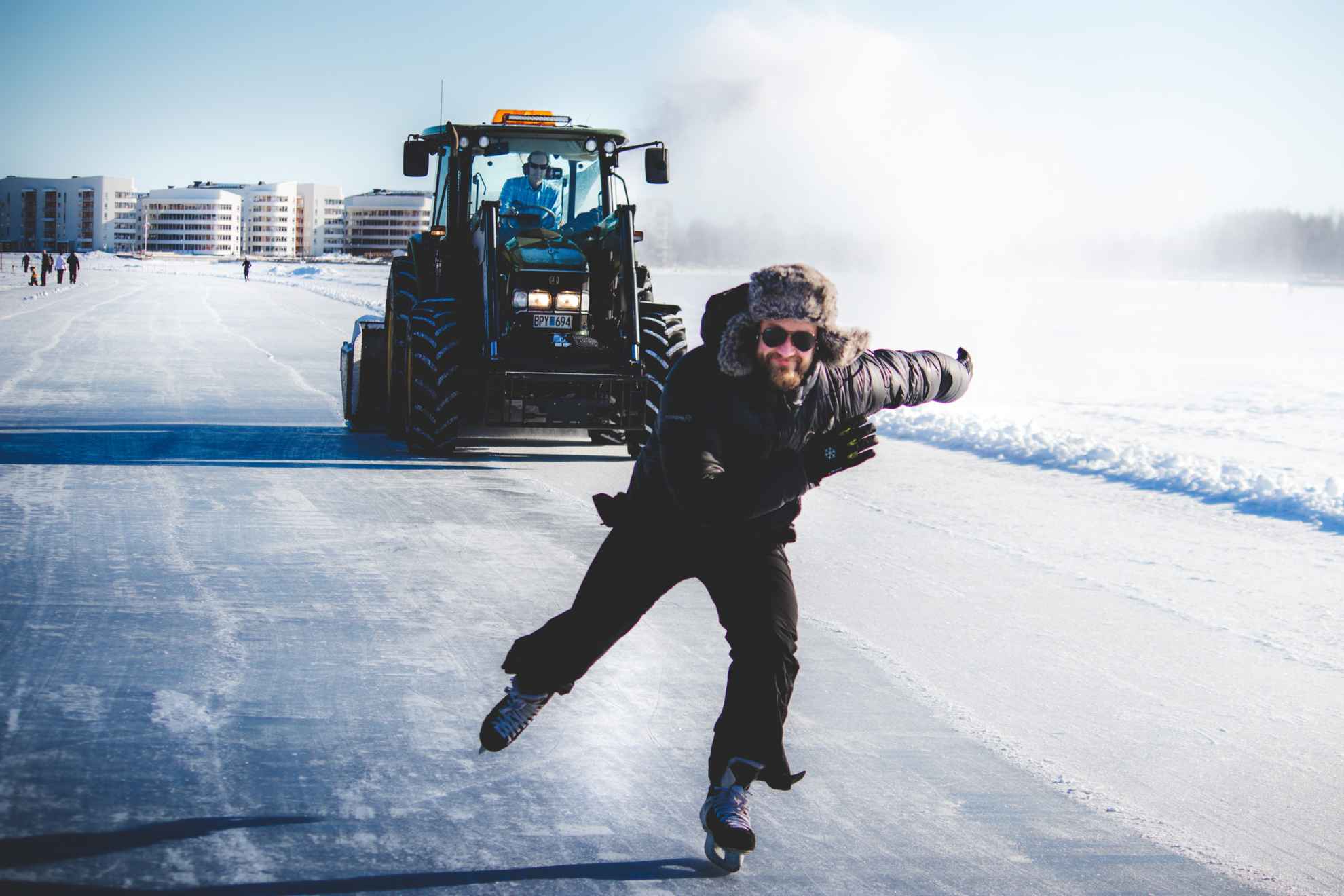 Ein schwarz gekleideter Mann, der auf dem Eis mit einem Traktor hinter ihm fährt