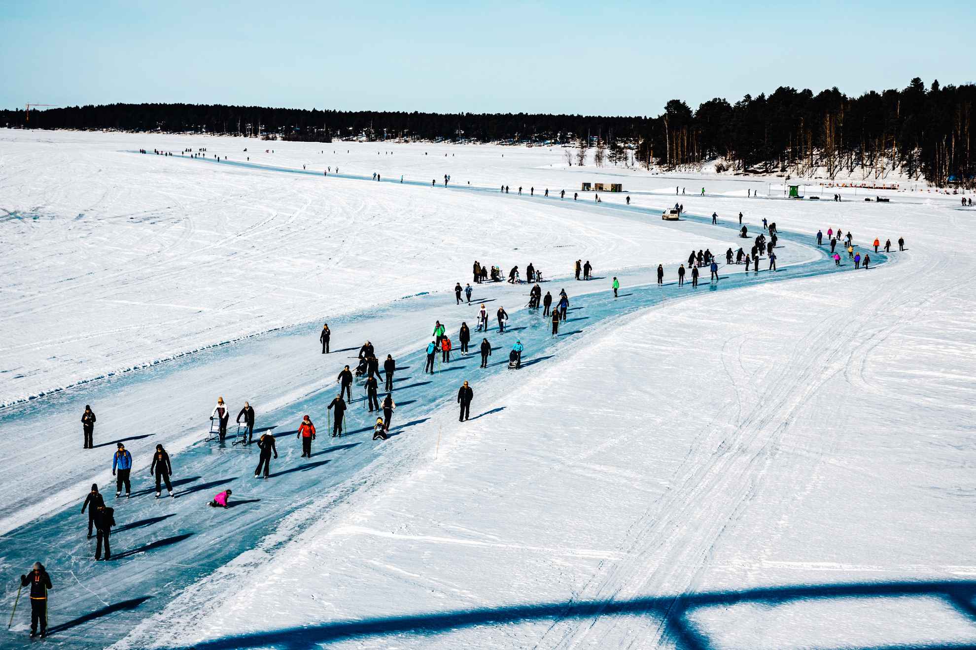Spaziergänger und Schlittschuhläufer auf der sonnigen Eisbahn rund um Luleå
